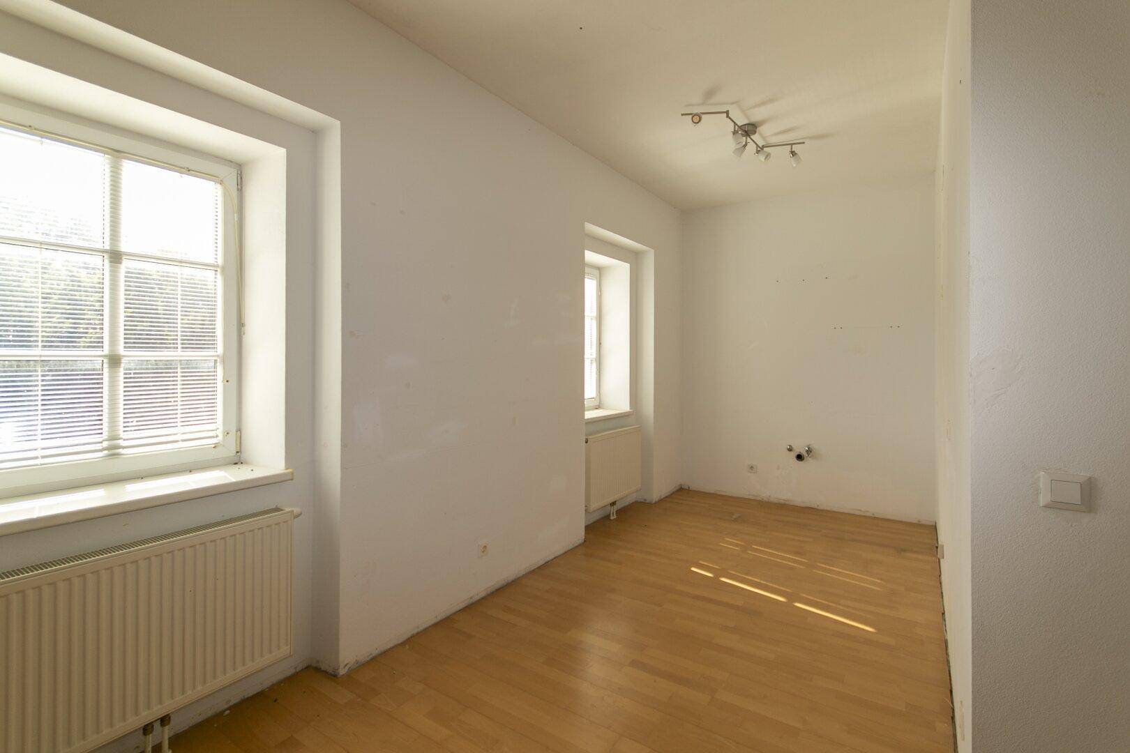 Lichtdurchfluteter Raum mit Parkettboden und zwei Fenstern, ideal für ein Wohn- oder Schlafzimmer.