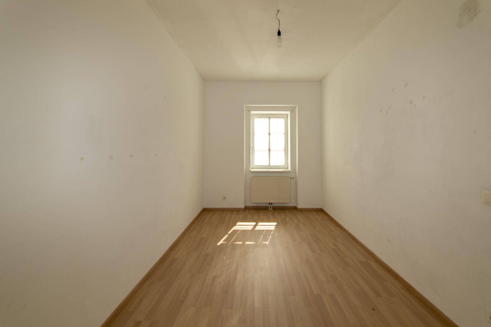 Schmaler, heller Raum mit Parkettboden und einem Fenster, geeignet als Schlaf- oder Arbeitszimmer.