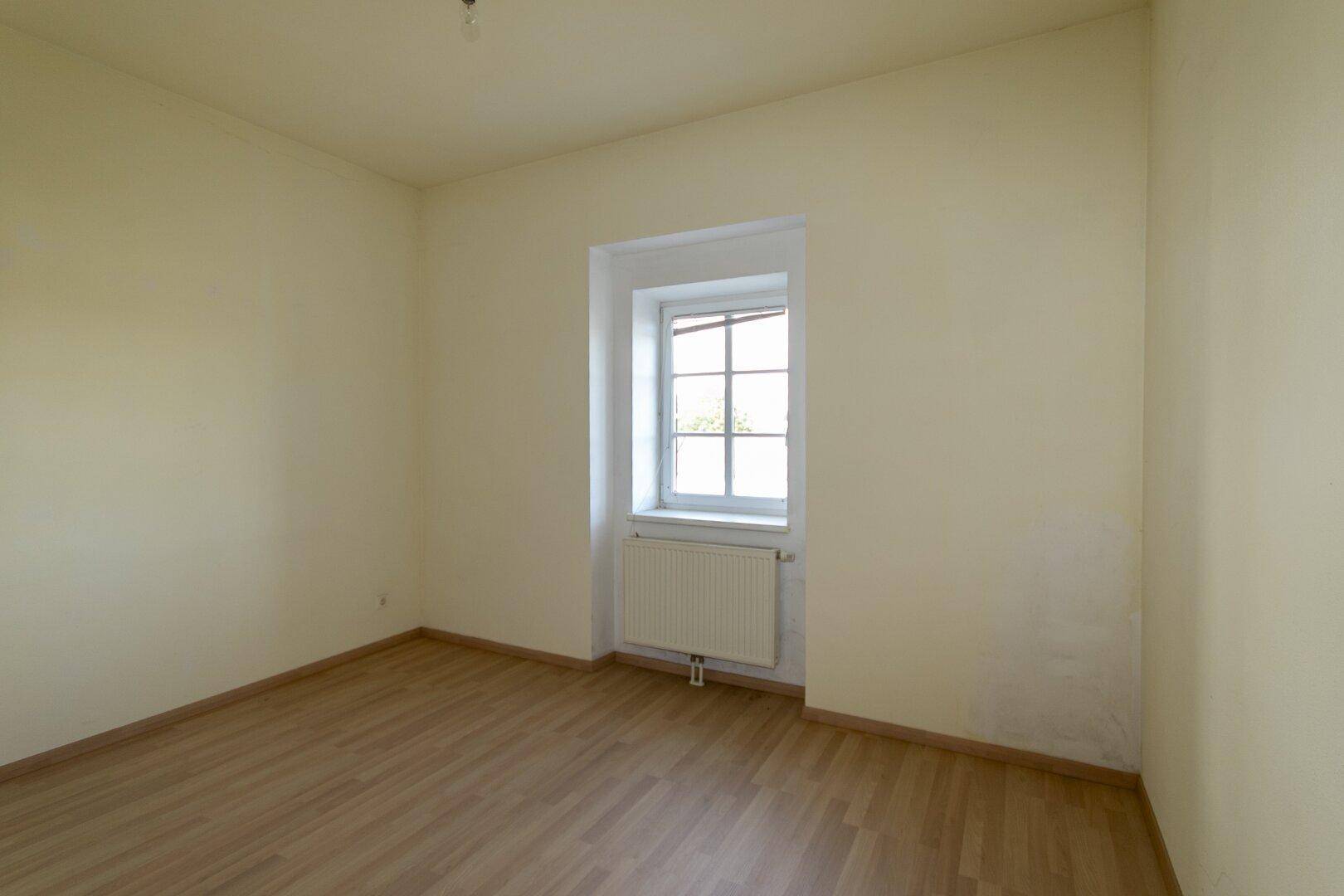 Helles Schlafzimmer mit hellgelben Wänden, Parkettboden und einem Fenster, bereit zur Einrichtung.