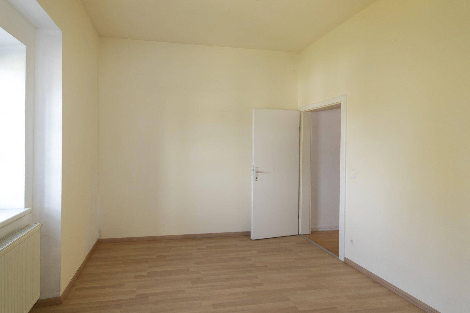 Geräumiges Schlafzimmer mit hellgelben Wänden, Parkettboden und Türzugang.