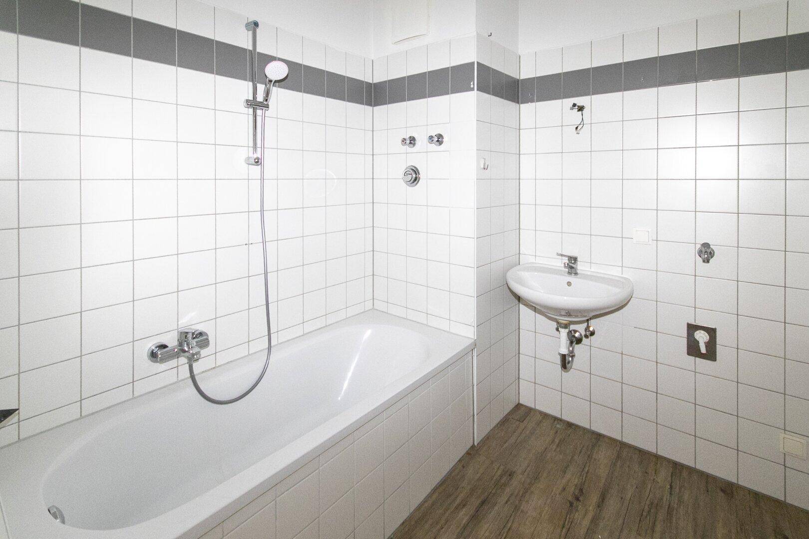 Badezimmer mit Badewanne, Waschbecken und weißen Fliesen, in gutem Zustand.