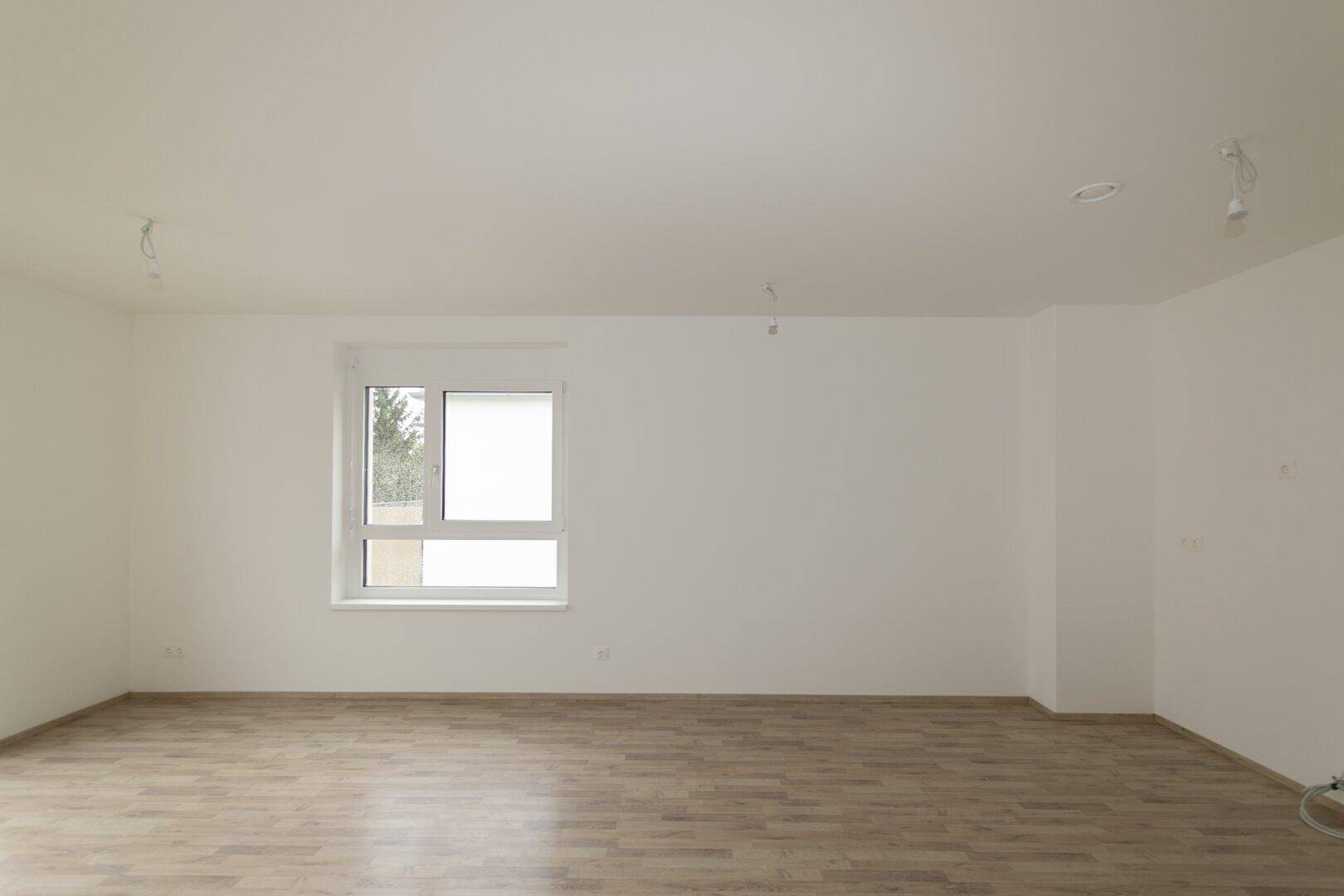 Großzügiges Wohnzimmer mit Laminatboden und einem großen Fenster, bereit zur individuellen Gestaltung.