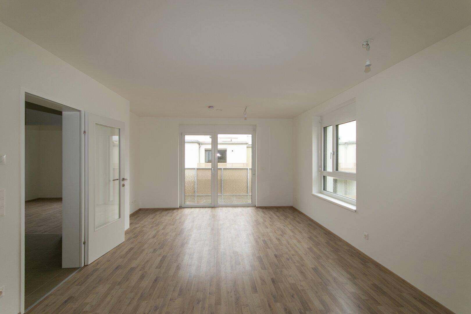 Helles Wohnzimmer mit Laminatboden und Zugang zu einem Balkon, ideal für neue Einrichtung.