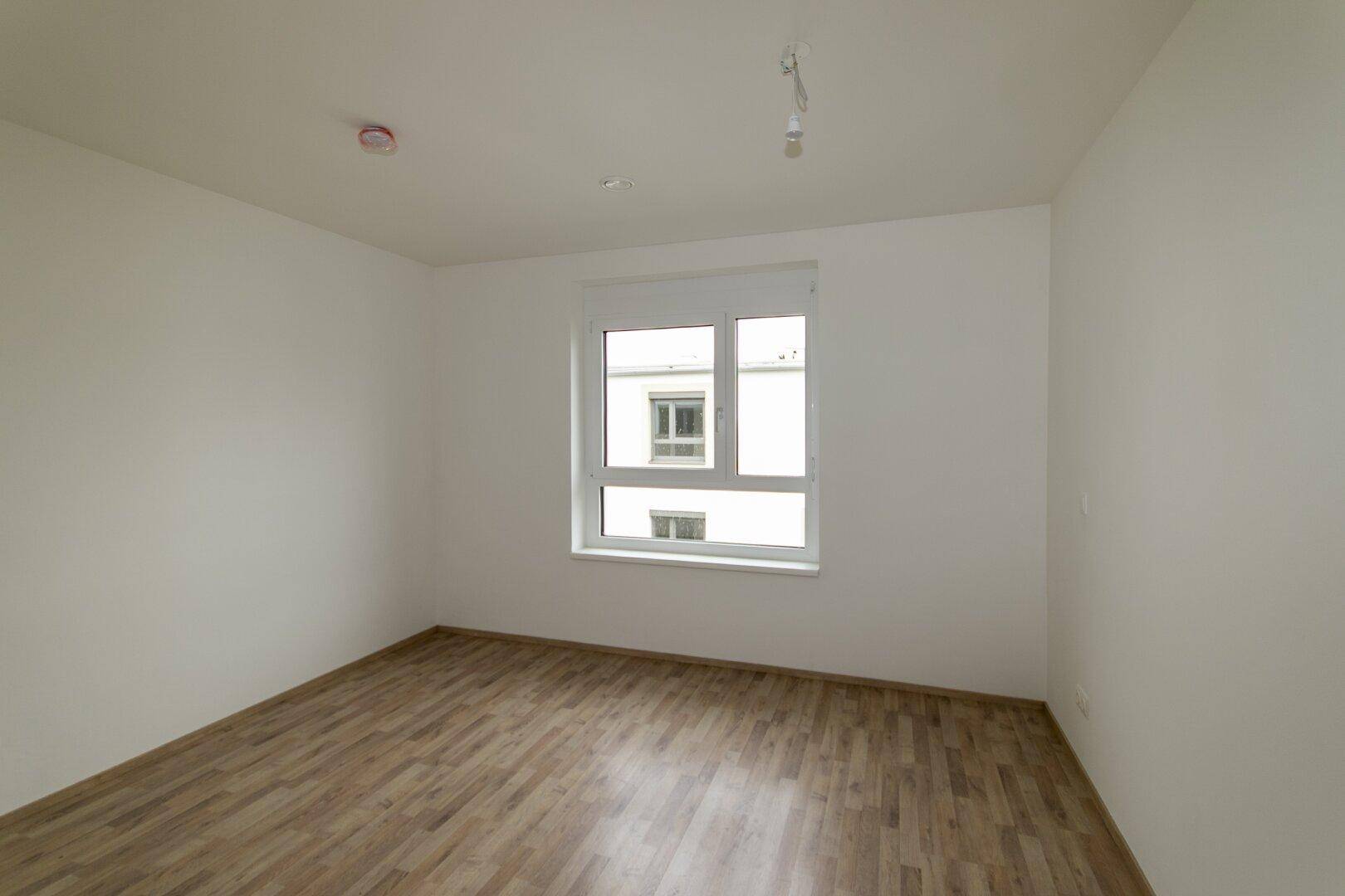 Helles Schlafzimmer mit Laminatboden und einem großen Fenster, bietet viel Tageslicht.