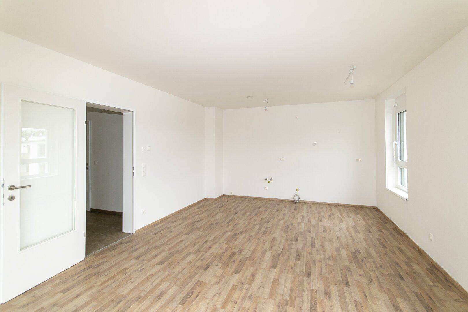 Leeres Wohnzimmer mit Laminatboden und weiß gestrichenen Wänden, bereit für die Einrichtung.