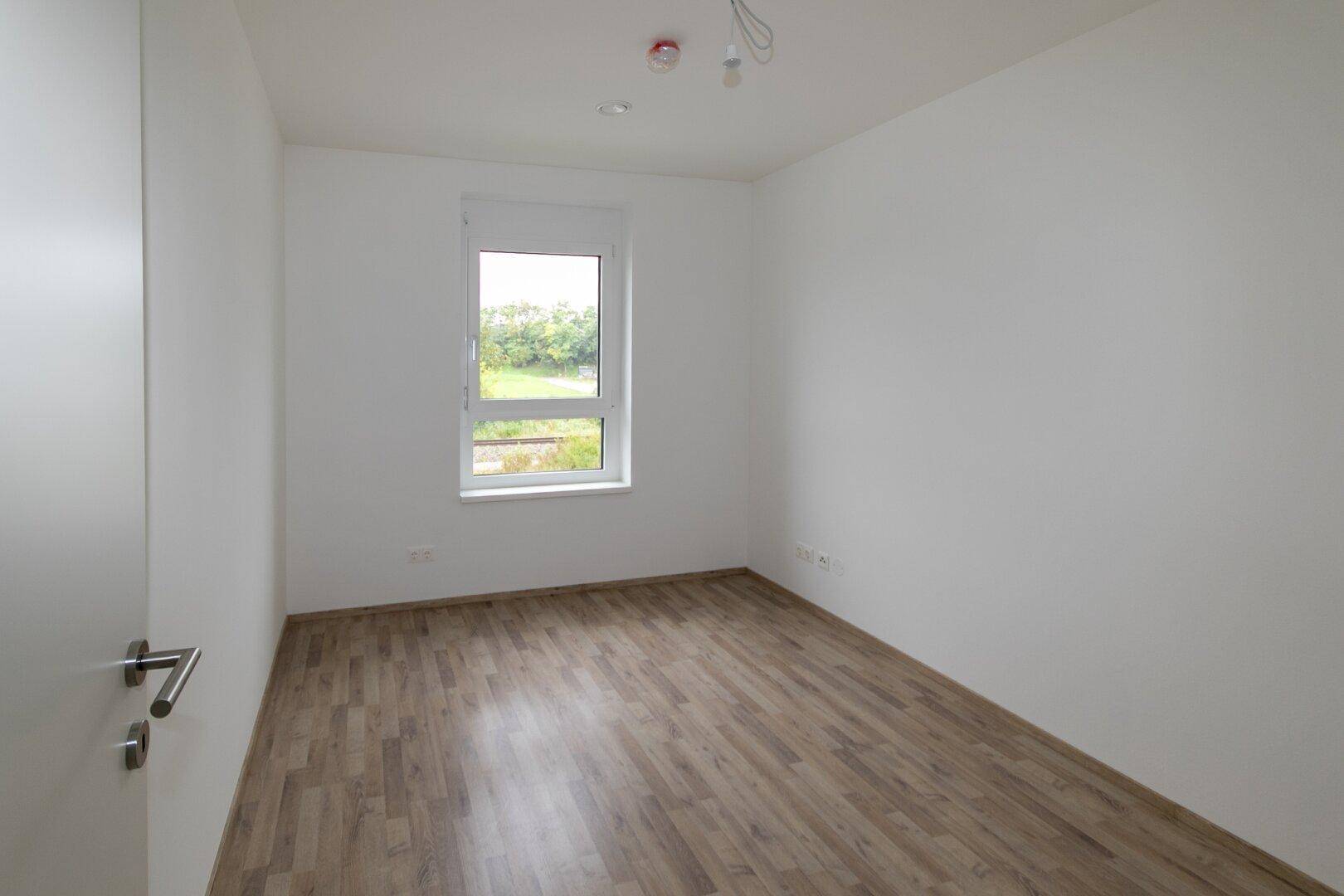 Unmöbliertes Schlafzimmer mit Laminatboden und einem Fenster, das viel Tageslicht hereinlässt.