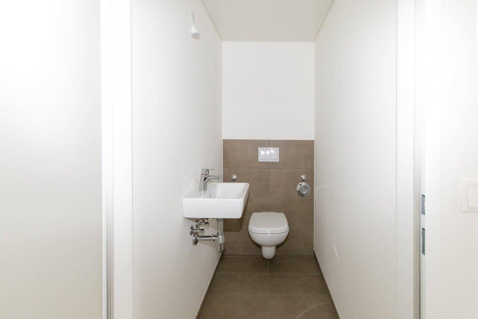 Modernes Gäste-WC mit Wand-WC und kleinem Waschbecken, halbhoch gefliest.