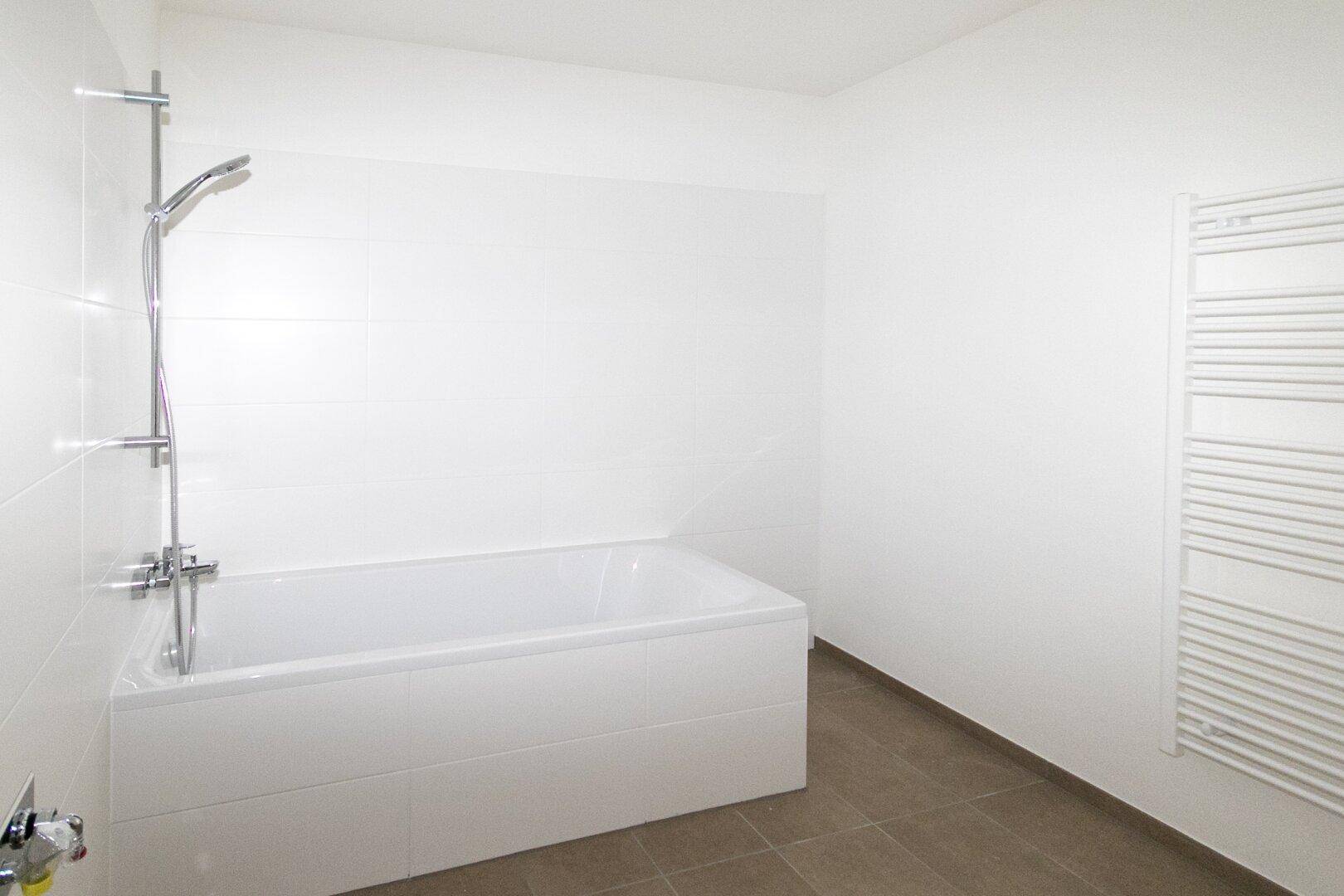 Badezimmer mit Badewanne und Duscharmatur, ausgestattet mit einem beheizten Handtuchhalter.