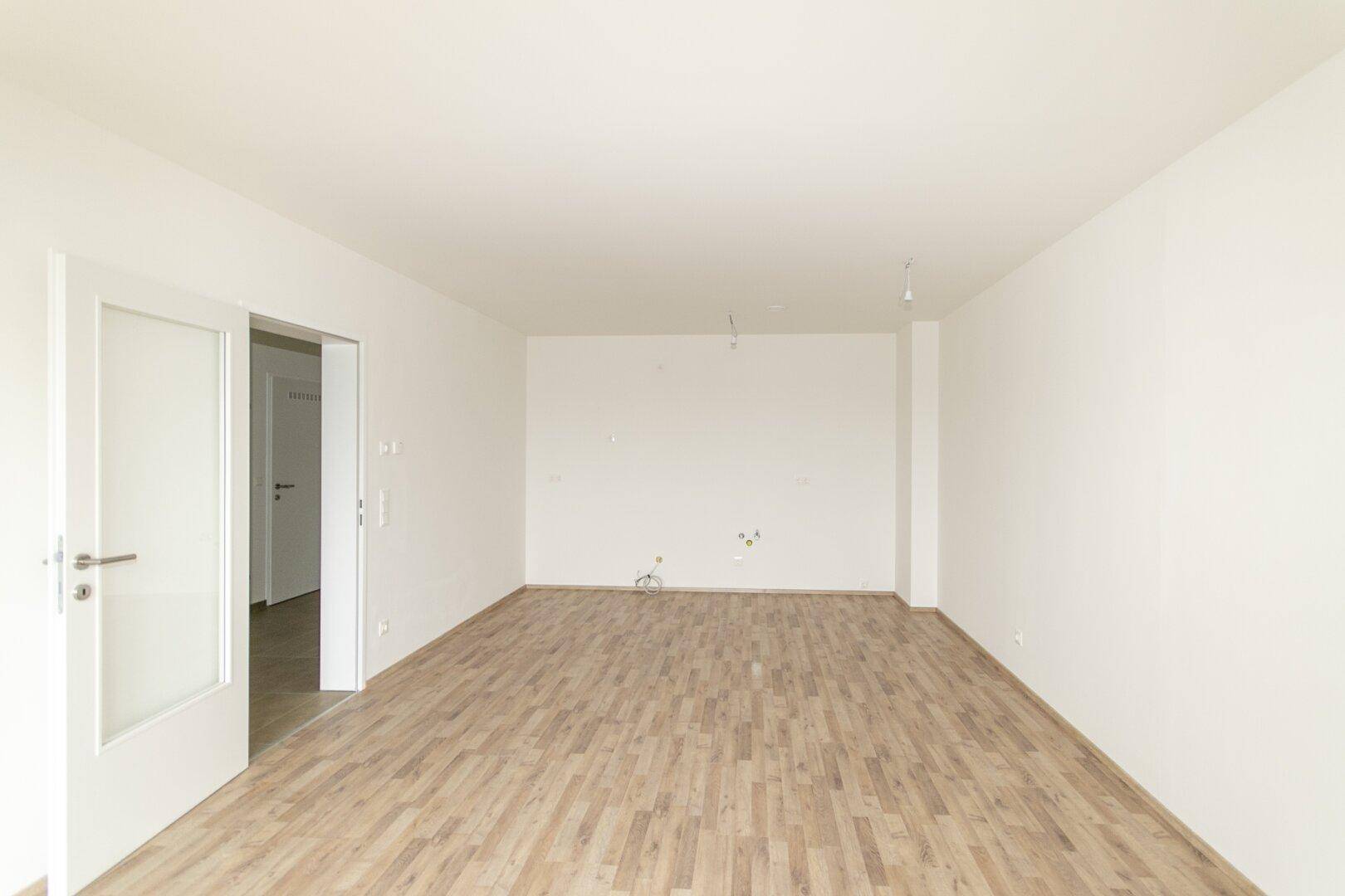 Helles, unmöbliertes Wohnzimmer mit Laminatboden und weiß gestrichenen Wänden, bereit zur Gestaltung.