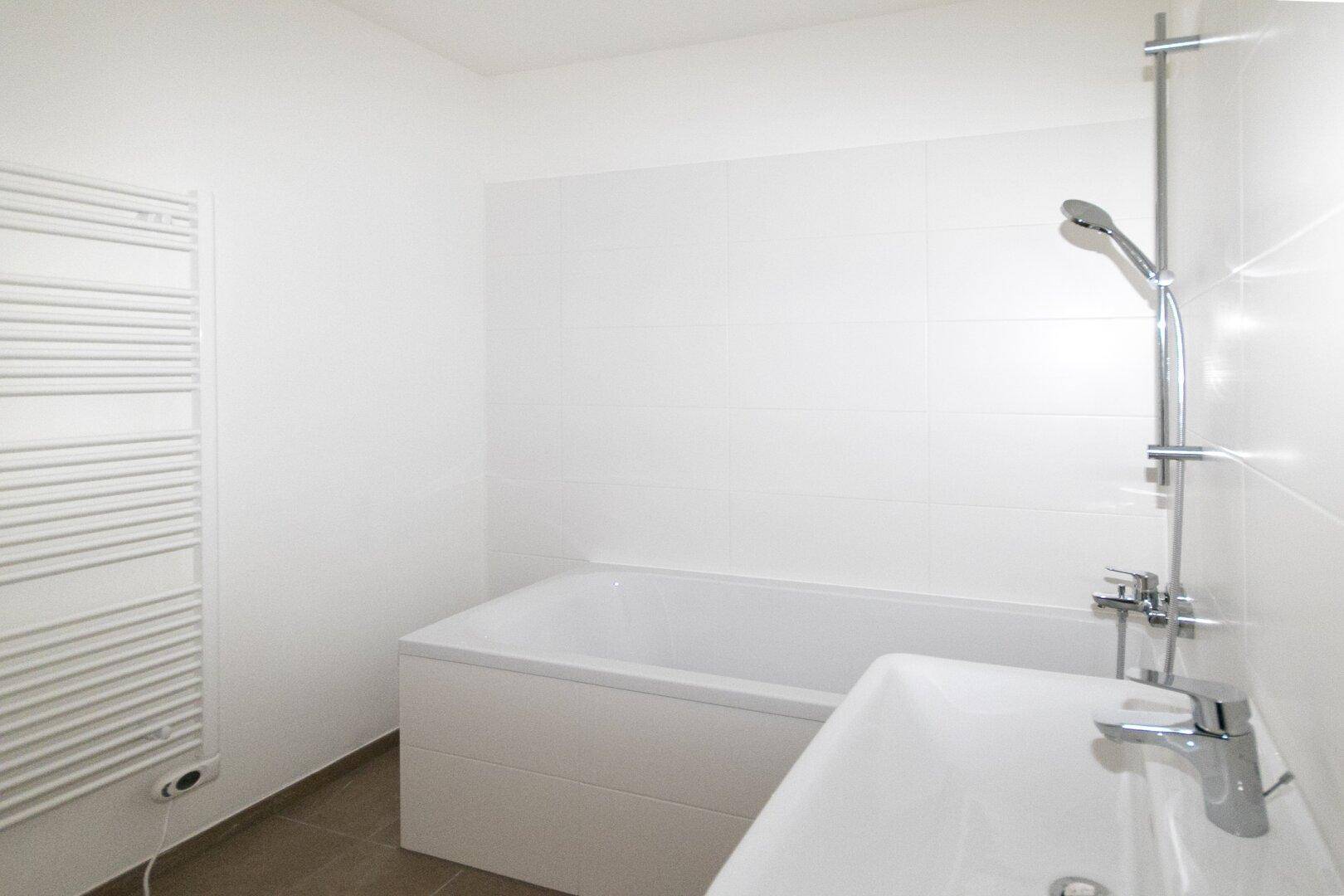 Helles Badezimmer mit Badewanne, Waschbecken und beheiztem Handtuchhalter, komplett gefliest.