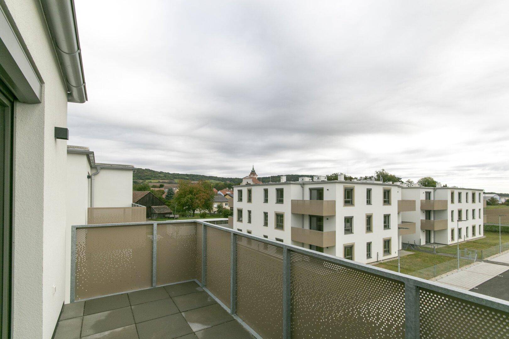 Blick vom Balkon auf die umliegenden Neubauten und die weite Landschaft unter bewölktem Himmel.