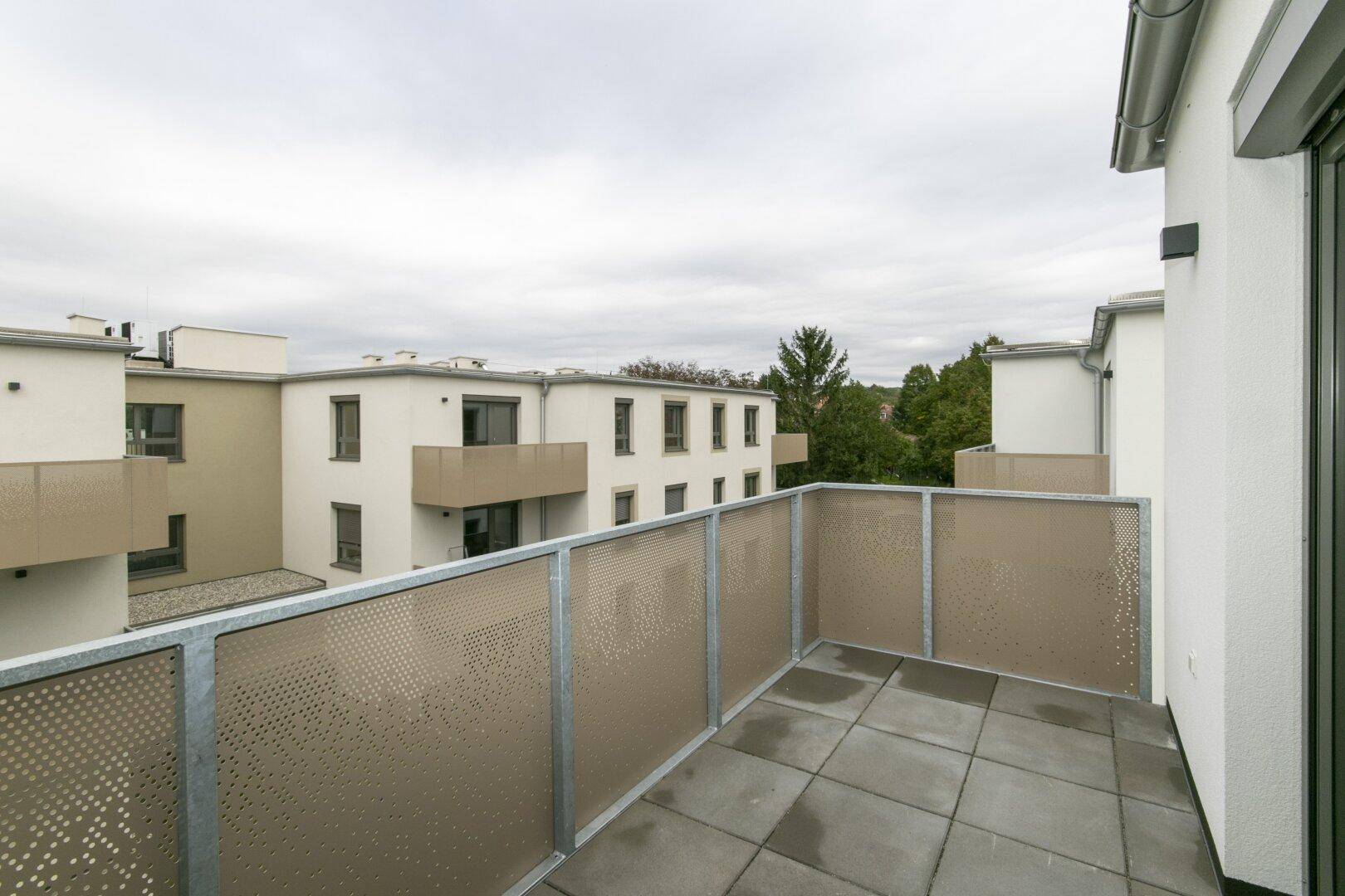 Geräumiger Balkon mit Fliesenboden und moderner Metallbrüstung, mit Blick auf Neubauten.