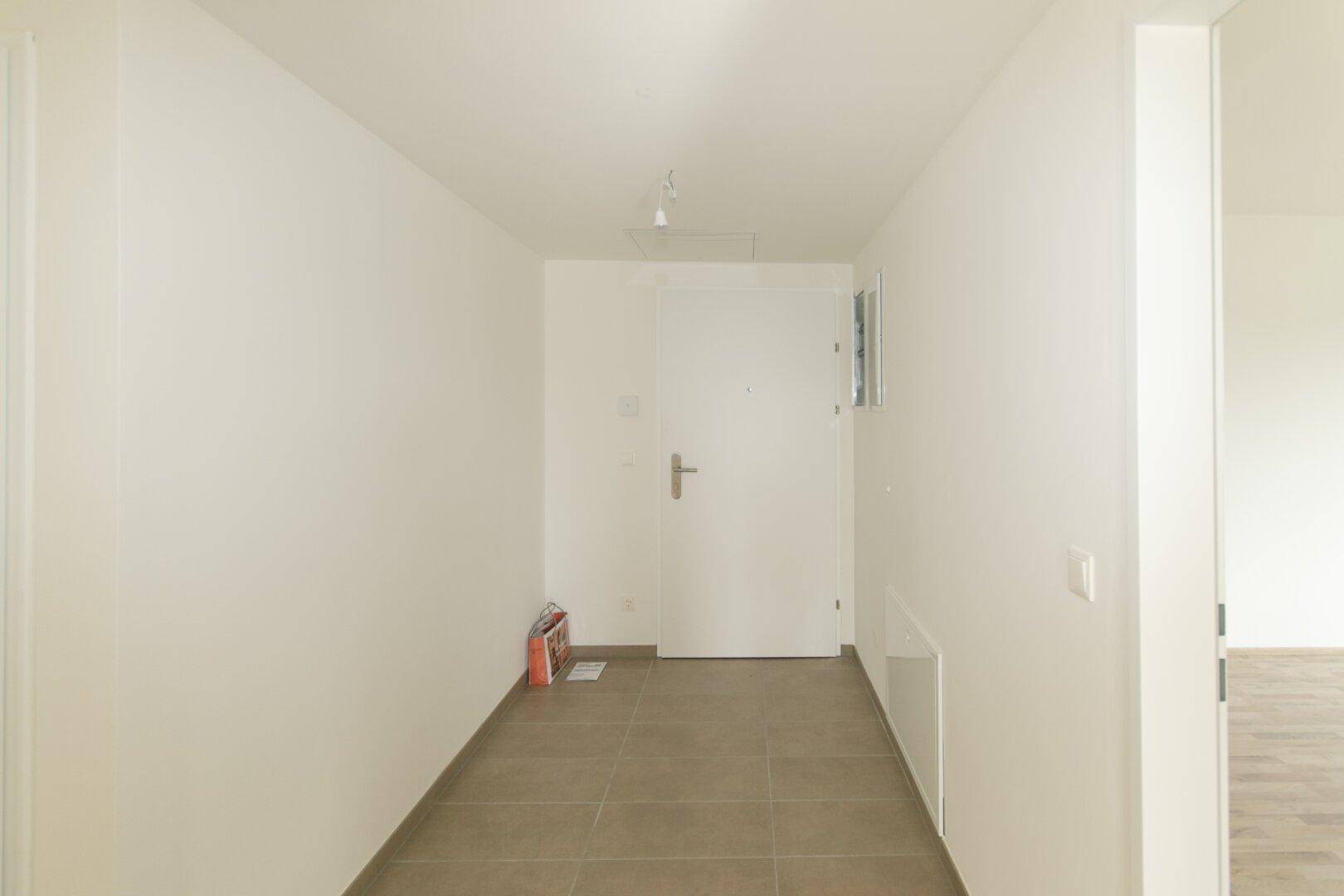 Eingangsbereich mit Fliesenboden und weißer Eingangstür in einem modernen Gebäude.