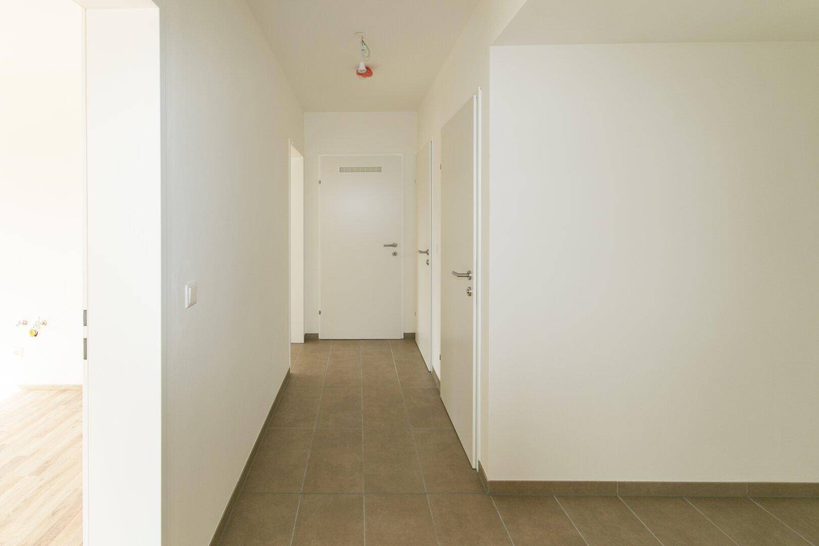 Langer, heller Flur mit Fliesenboden und mehreren weißen Türen zu den Zimmern.