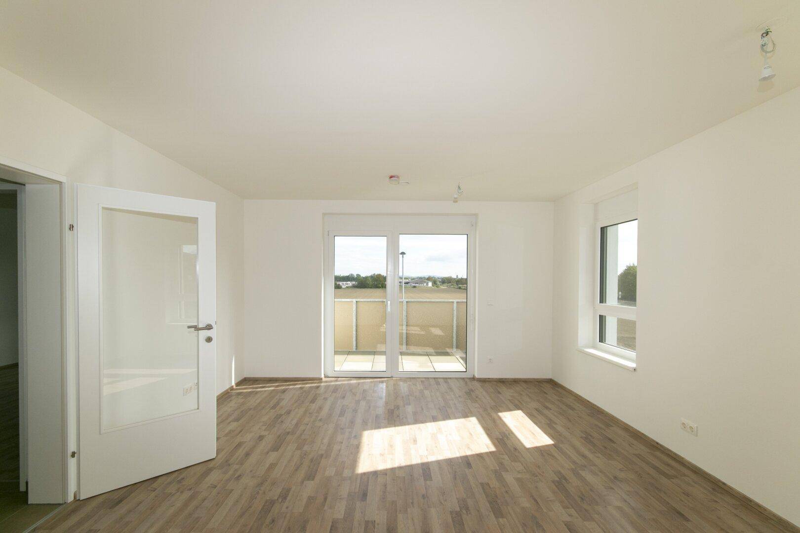 Heller Wohnraum mit Laminatboden und Balkonzugang, durch eine Glastür erreichbar.