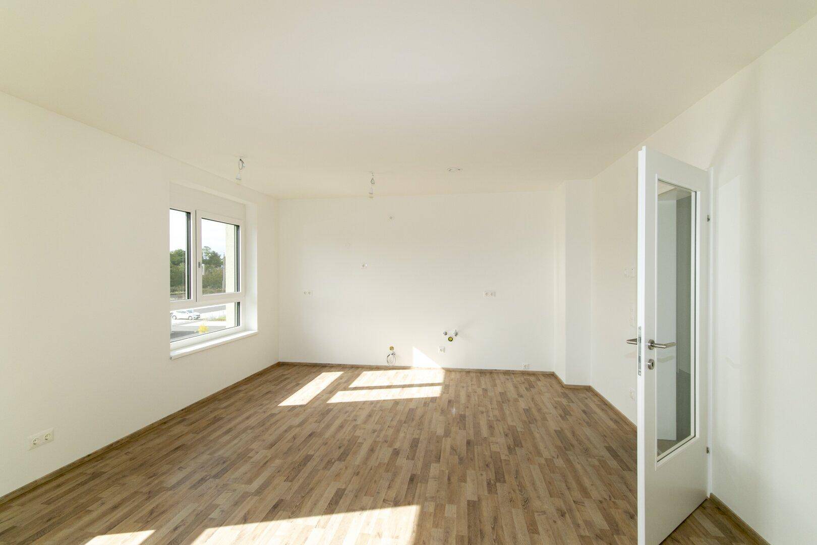 Heller Küchenbereich mit Laminatboden und Fenster, bereit für die Installation einer Einbauküche.