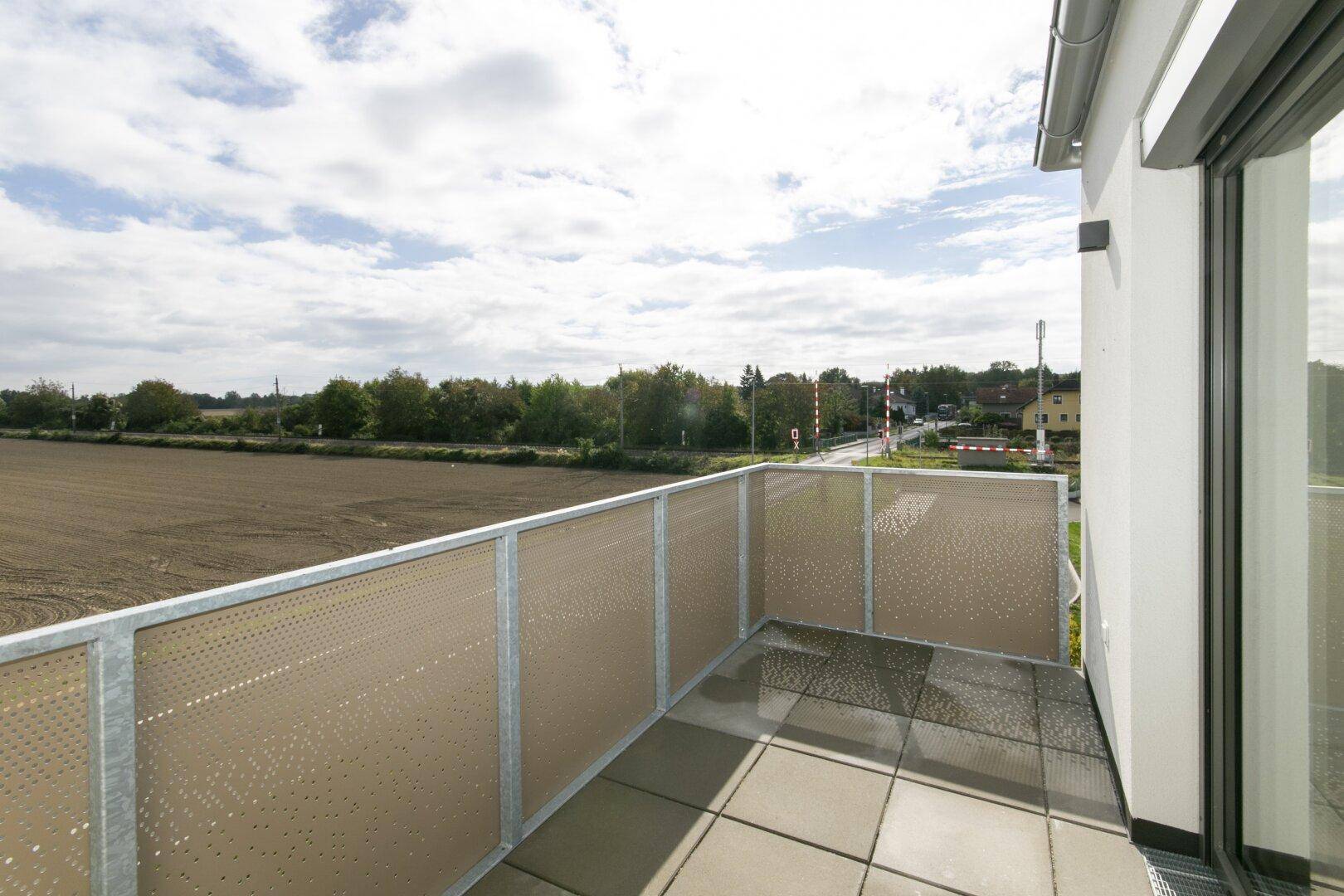 Balkon mit Fliesenboden und Metallgeländer, bietet Blick auf Felder und eine Straße.