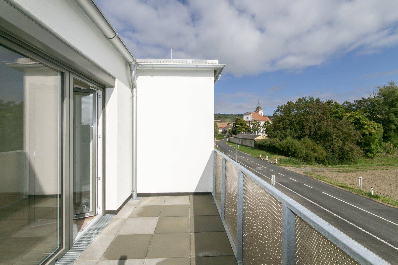 Heller Balkon mit Fliesenboden und weitem Blick auf die Straße und ein Dorf.