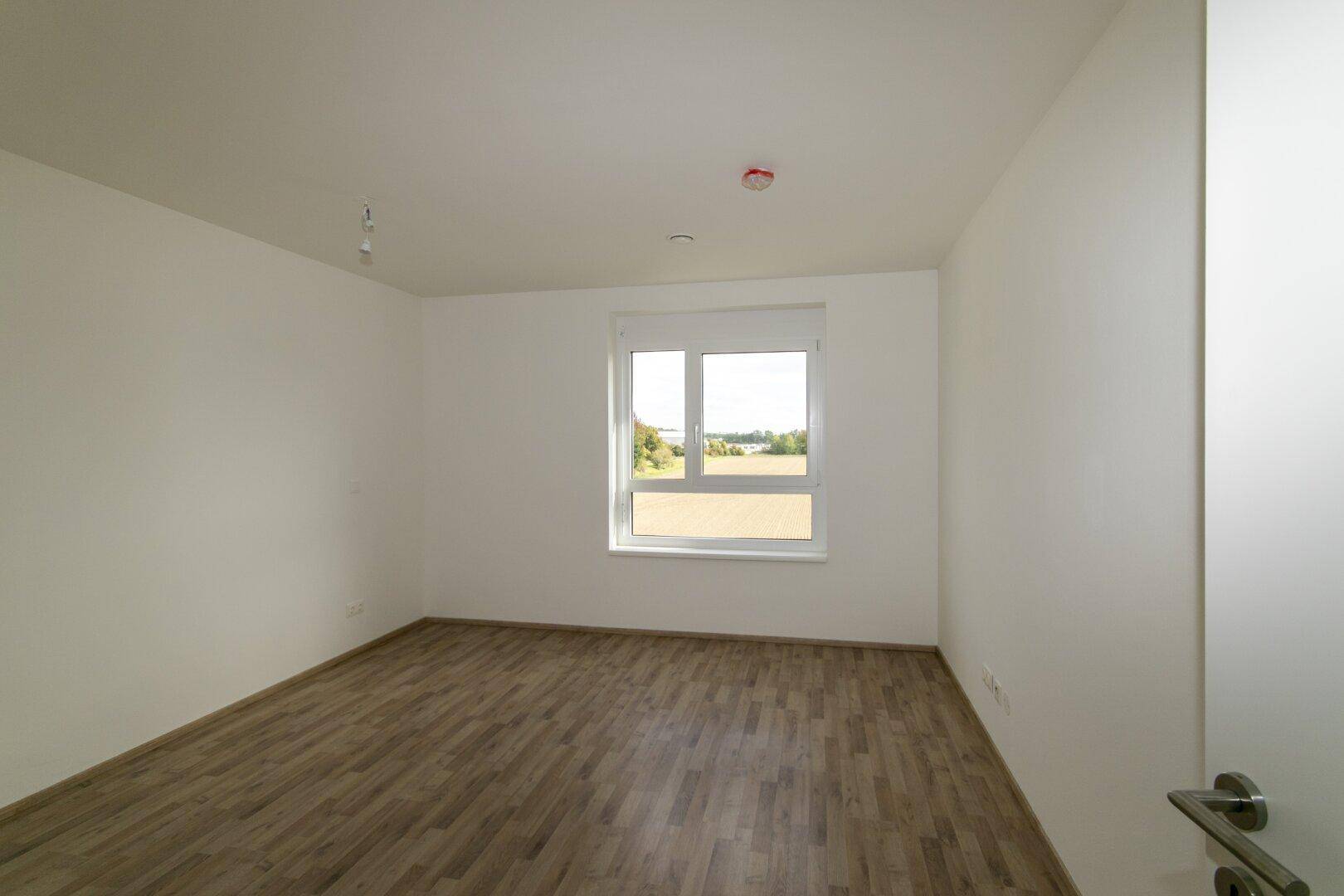 Helles Schlafzimmer mit Laminatboden und einem Fenster, das viel Tageslicht hereinlässt.