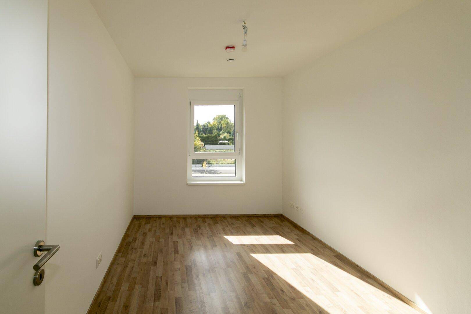 Geräumiges Schlafzimmer mit Laminatboden und sonnigem Fenster, ideal für natürliche Beleuchtung.