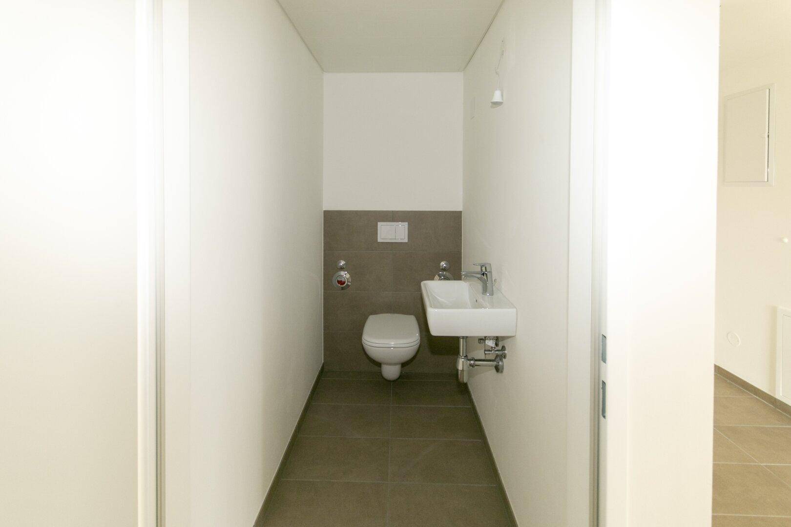 Kompaktes Gäste-WC mit wandhängender Toilette und kleinem Waschbecken, modern gefliest.