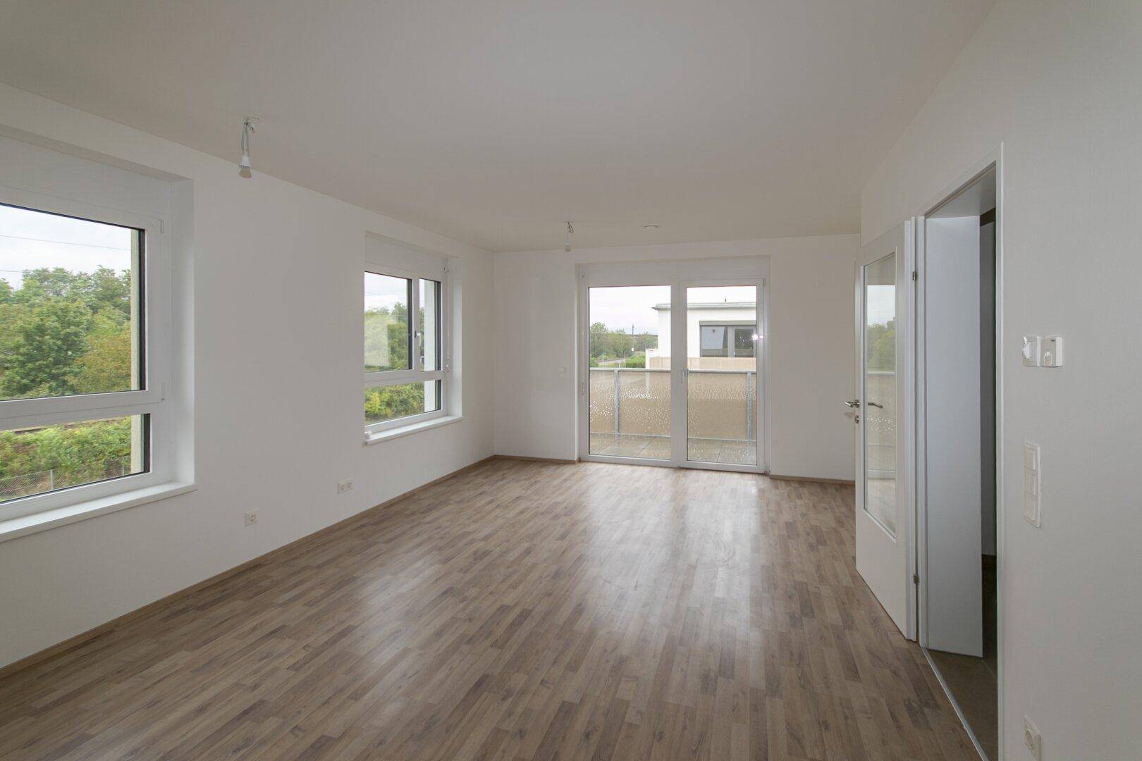 Helles, leeres Zimmer mit Laminatboden und Zugang zu einem Balkon, ideal als Wohnbereich.