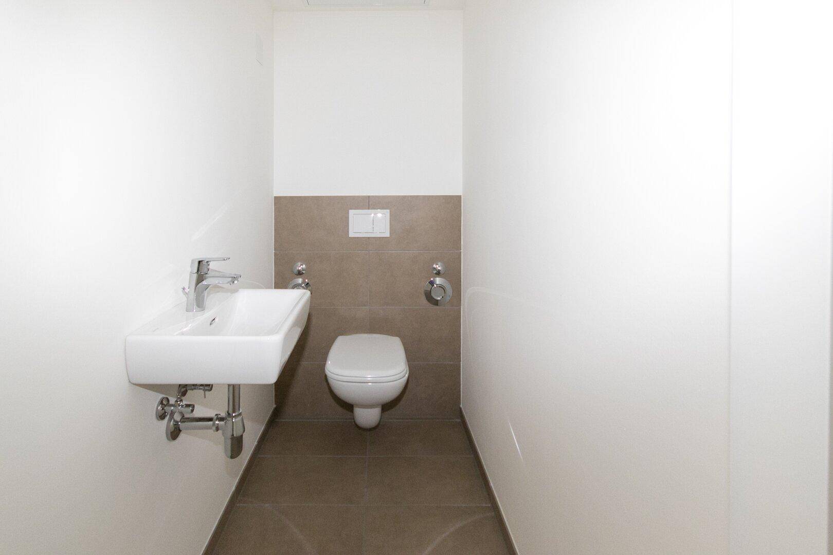 Kleines Gäste-WC mit wandhängender Toilette und Handwaschbecken, in modernen Farben gehalten.