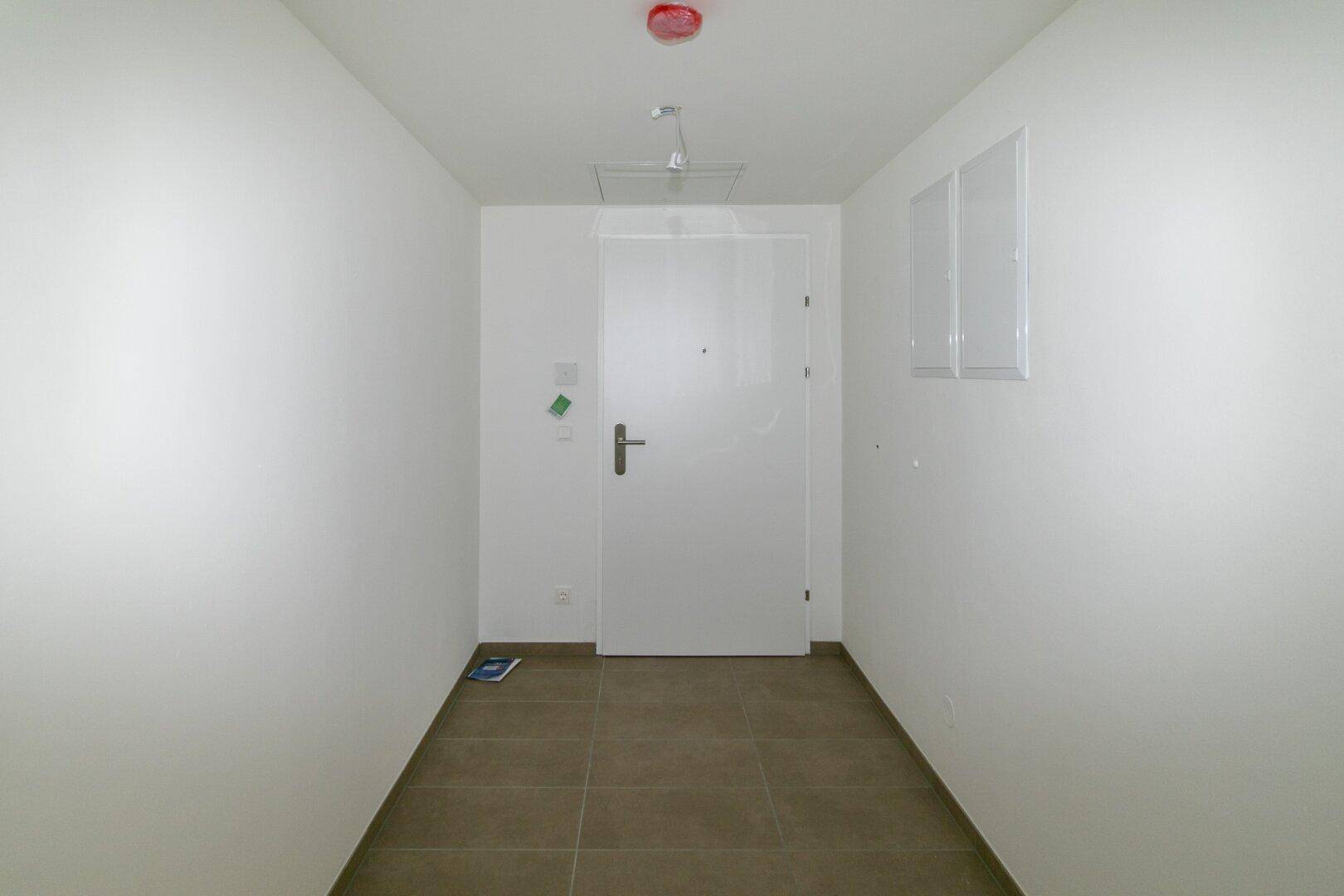 Geräumiger Eingangsbereich mit Fliesenboden und weißer Eingangstür in einem modernen Gebäude.