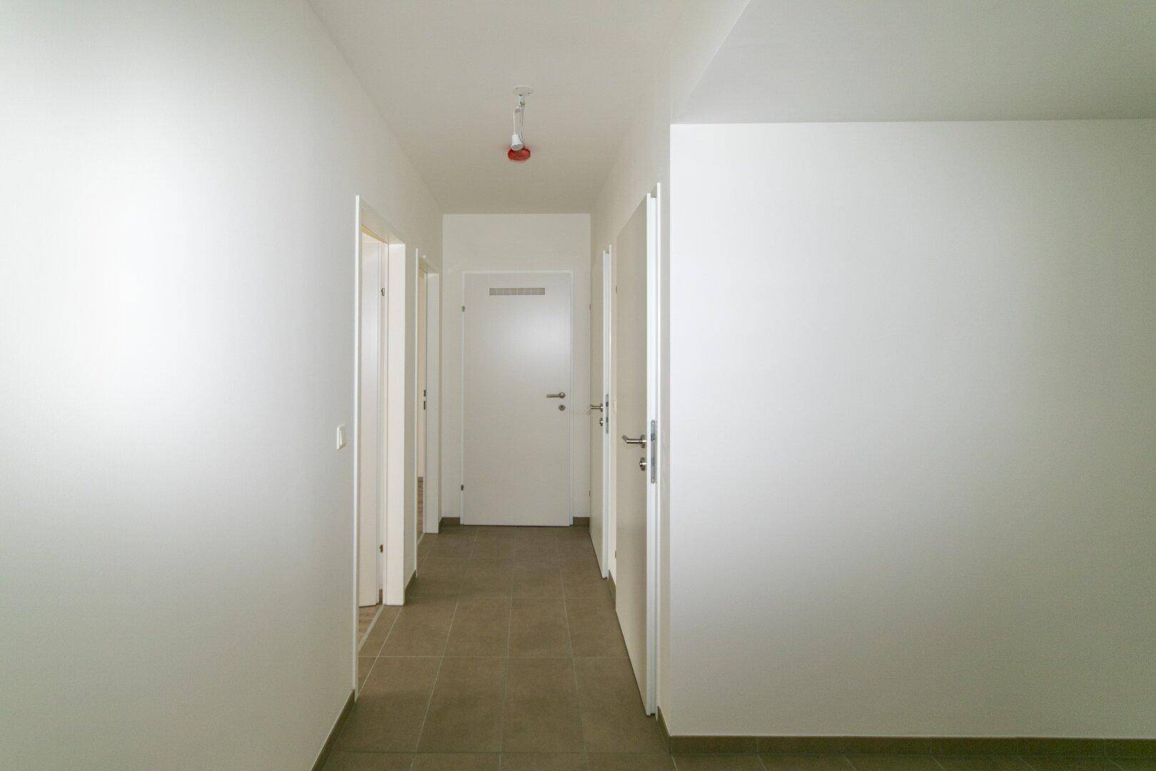 Langer, heller Flur mit Fliesenboden und mehreren Türen zu den angrenzenden Zimmern.