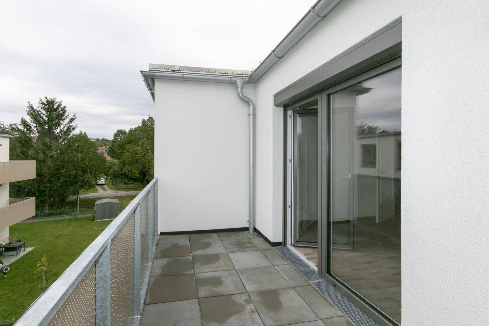 Balkon mit Fliesenboden und Blick auf die grüne Umgebung und angrenzende Gebäude.