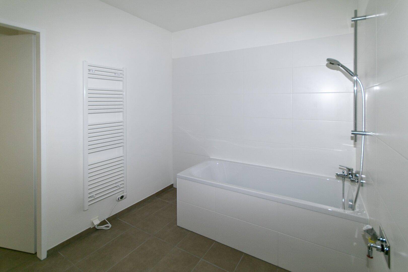 Helles Badezimmer mit Badewanne, Handtuchheizkörper und Fliesenboden.