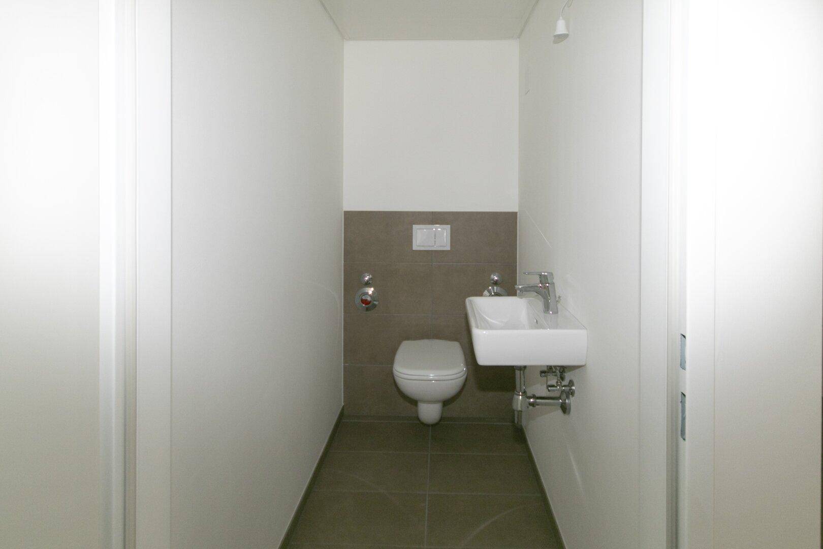 Gäste-WC mit wandhängender Toilette, kleinem Waschbecken und Fliesenboden.