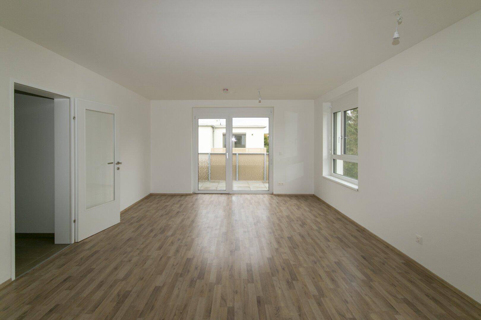 Großes, helles Zimmer mit Laminatboden und Balkonzugang, bereit für individuelle Gestaltung.