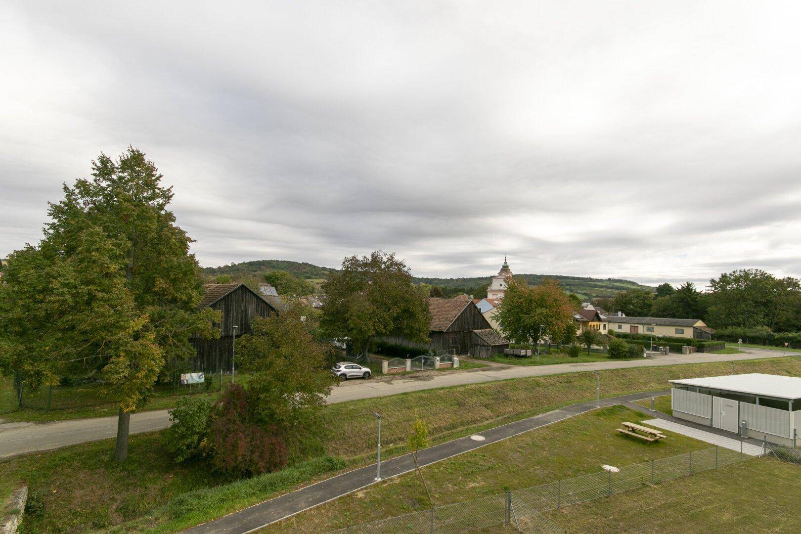 Weitläufiger Blick über die ländliche Umgebung mit Bäumen, Feldern und einem Dorf im Hintergrund.
