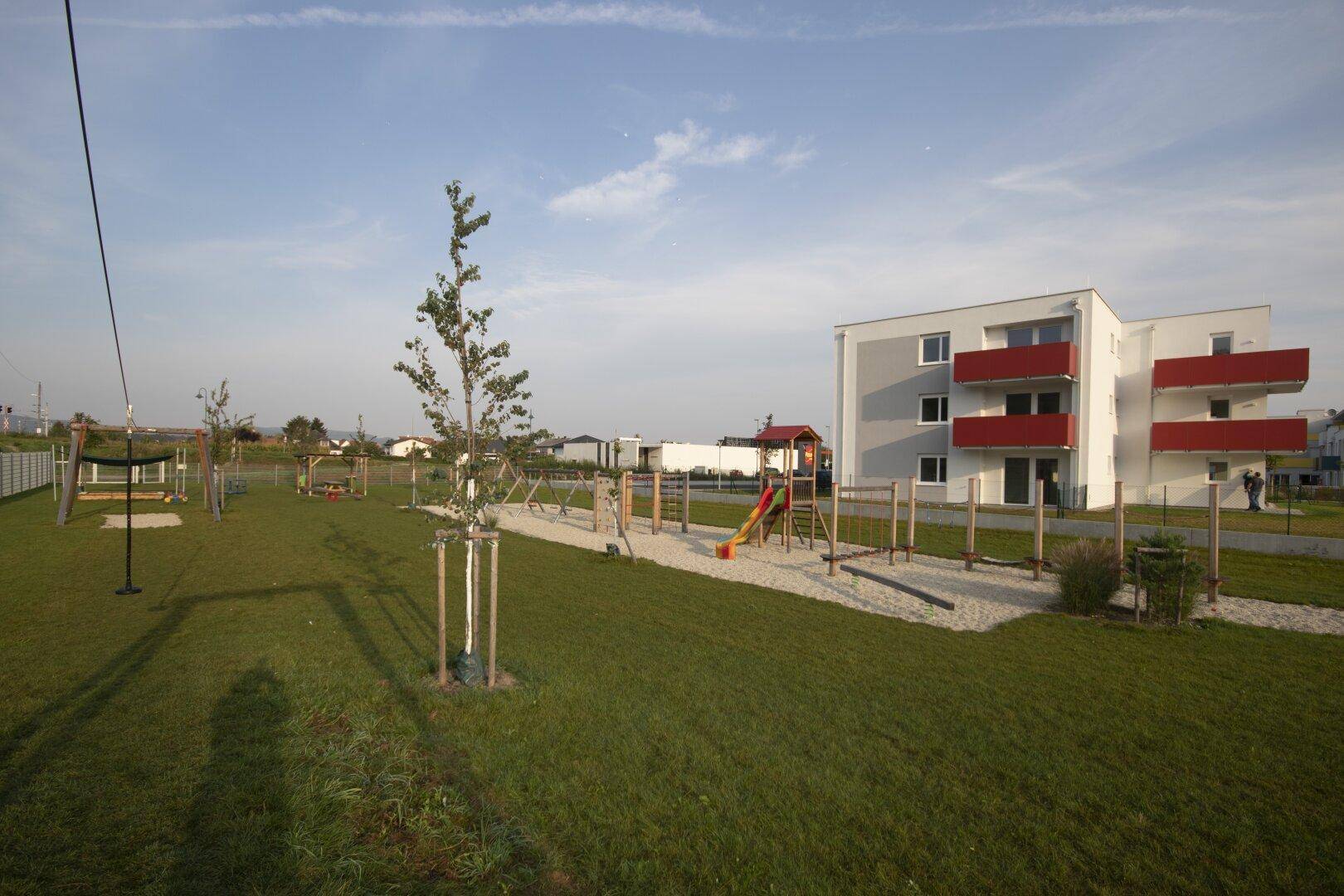 Großer Kinderspielplatz mit Rutsche und Schaukeln neben einem Wohngebäude.