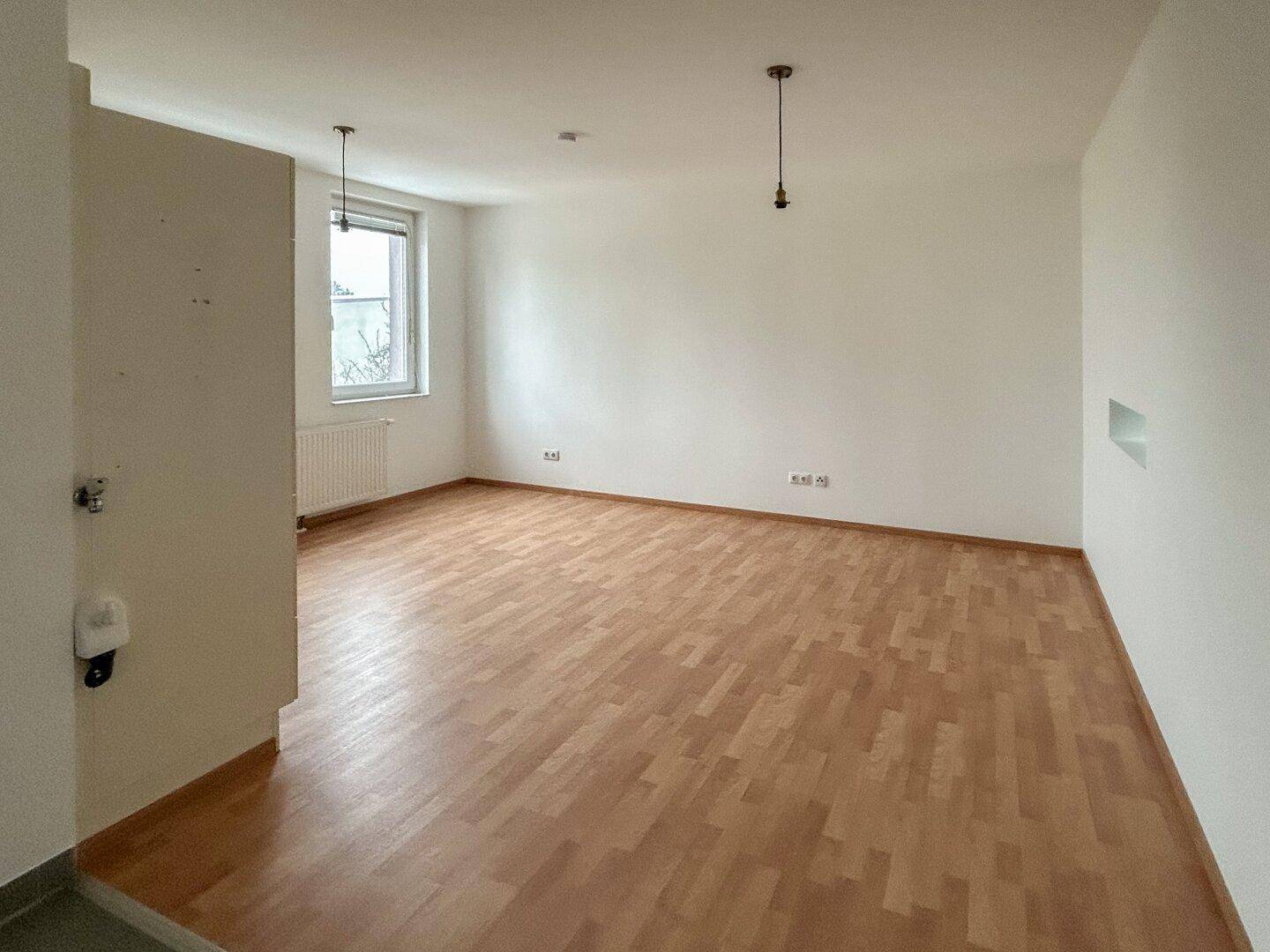 Geräumiger, heller Raum mit Laminatboden, weißen Wänden und einem Fenster.