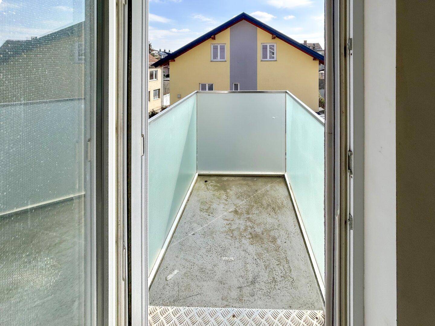Blick von innen auf eine kleine Loggia mit Milchglaswänden und einem Gebäude im Hintergrund.