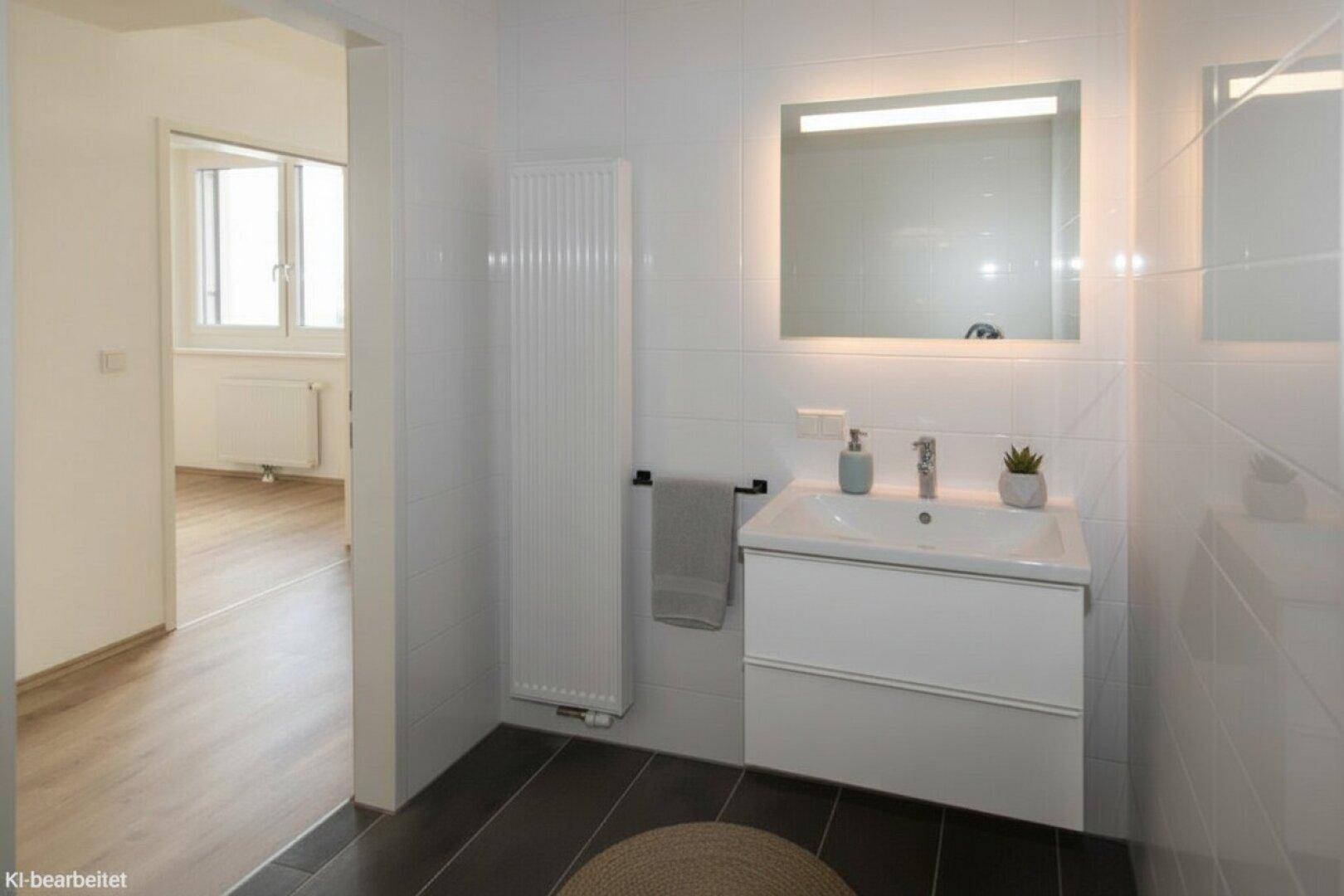 Modernes Badezimmer mit Waschtisch, beleuchtetem Spiegel und Handtuchheizkörper.