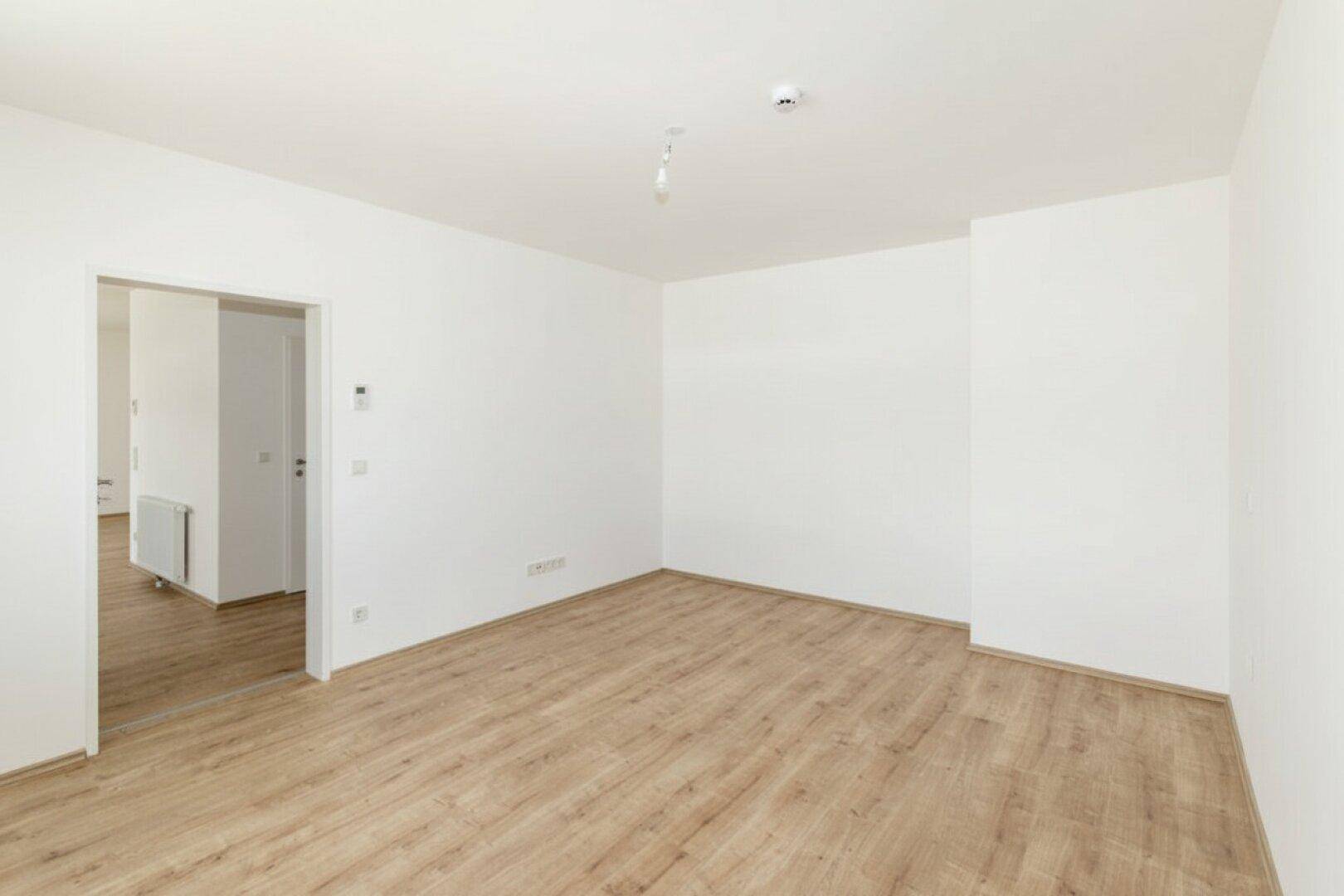 Leerer, heller Raum mit Laminatboden und Zugang zu einem weiteren Zimmer, vielseitig nutzbar.