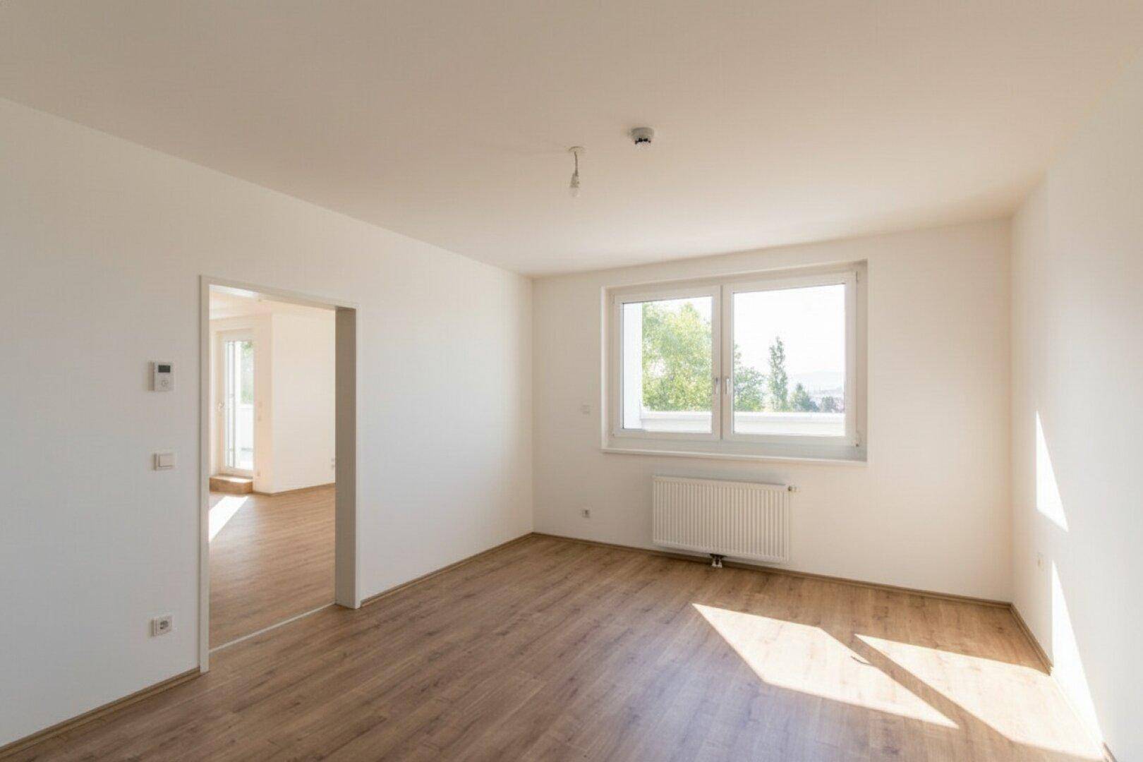 Lichtdurchfluteter Wohnraum mit Laminatboden und großem Fenster, bereit zum Einzug.
