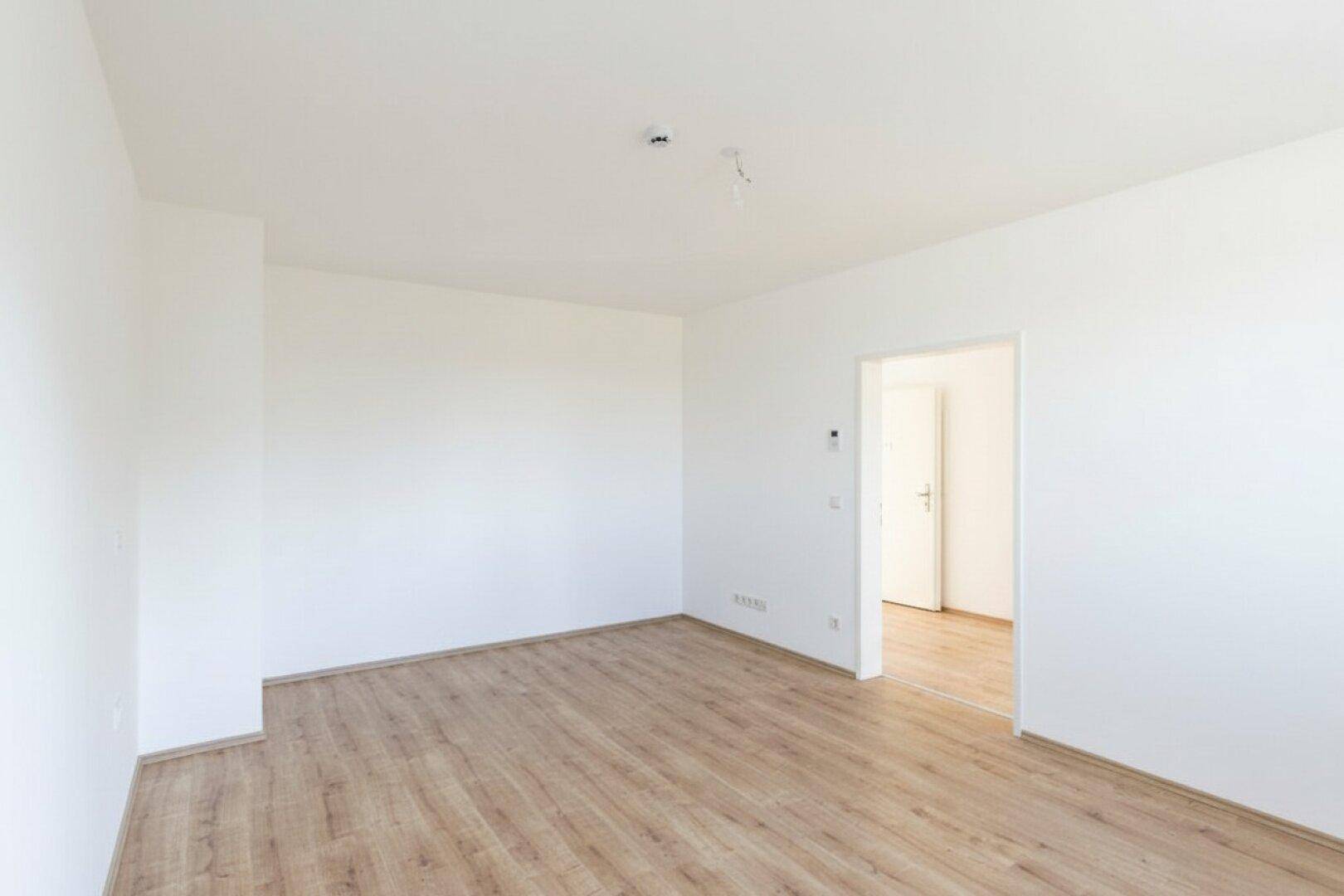 Heller, leerer Wohnraum mit Laminatboden und weiß gestrichenen Wänden.