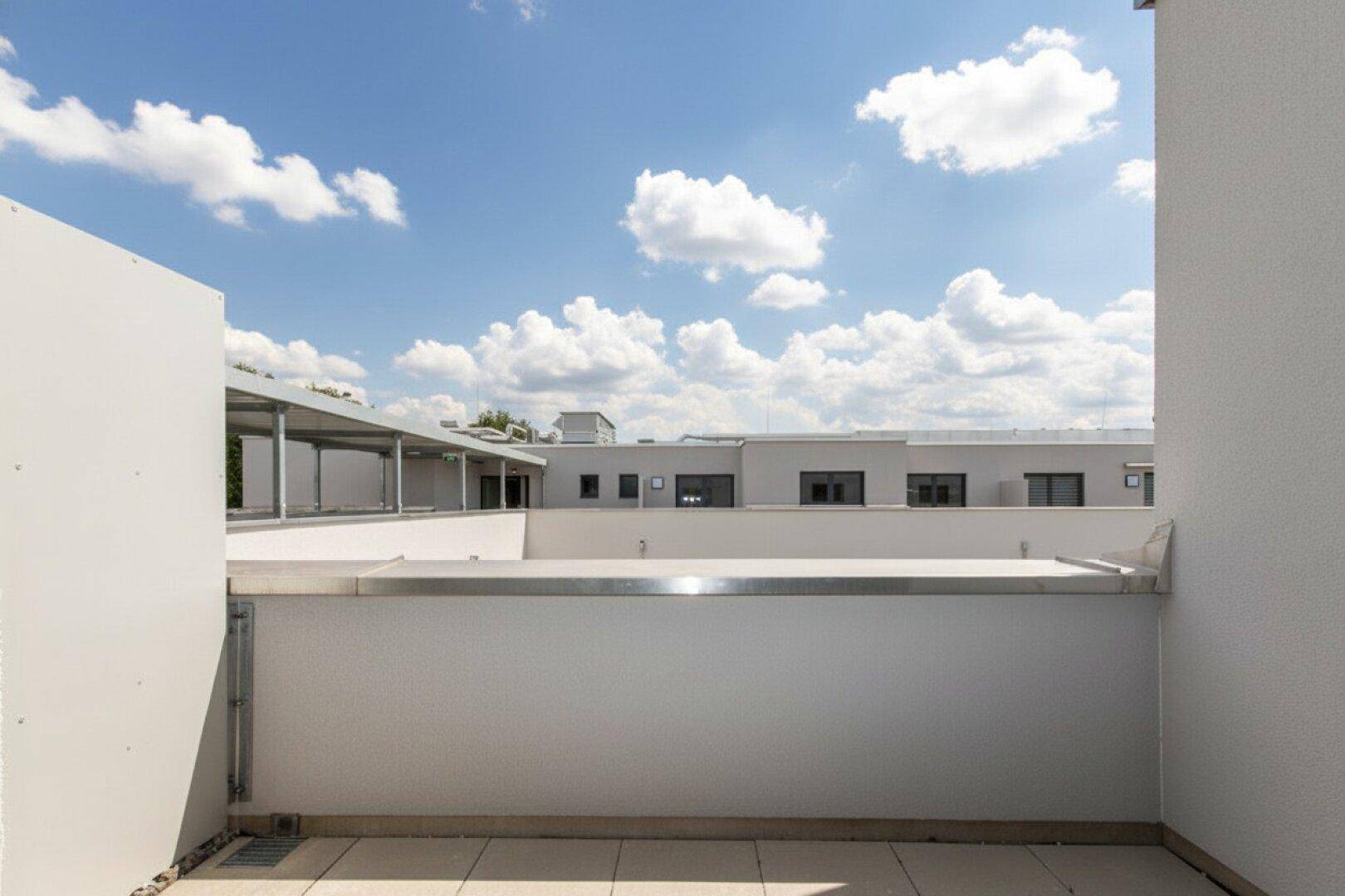 Geräumiger Balkon mit Fliesen und weitem Blick auf die moderne Wohnanlage bei sonnigem Wetter.