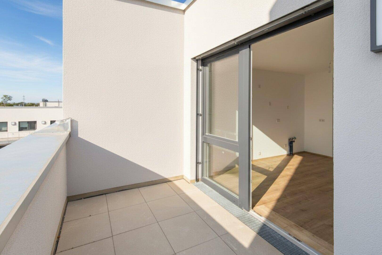 Sonniger Balkon mit Fliesenboden und großer Schiebetür, die Zugang zu einem hellen Innenraum bietet.