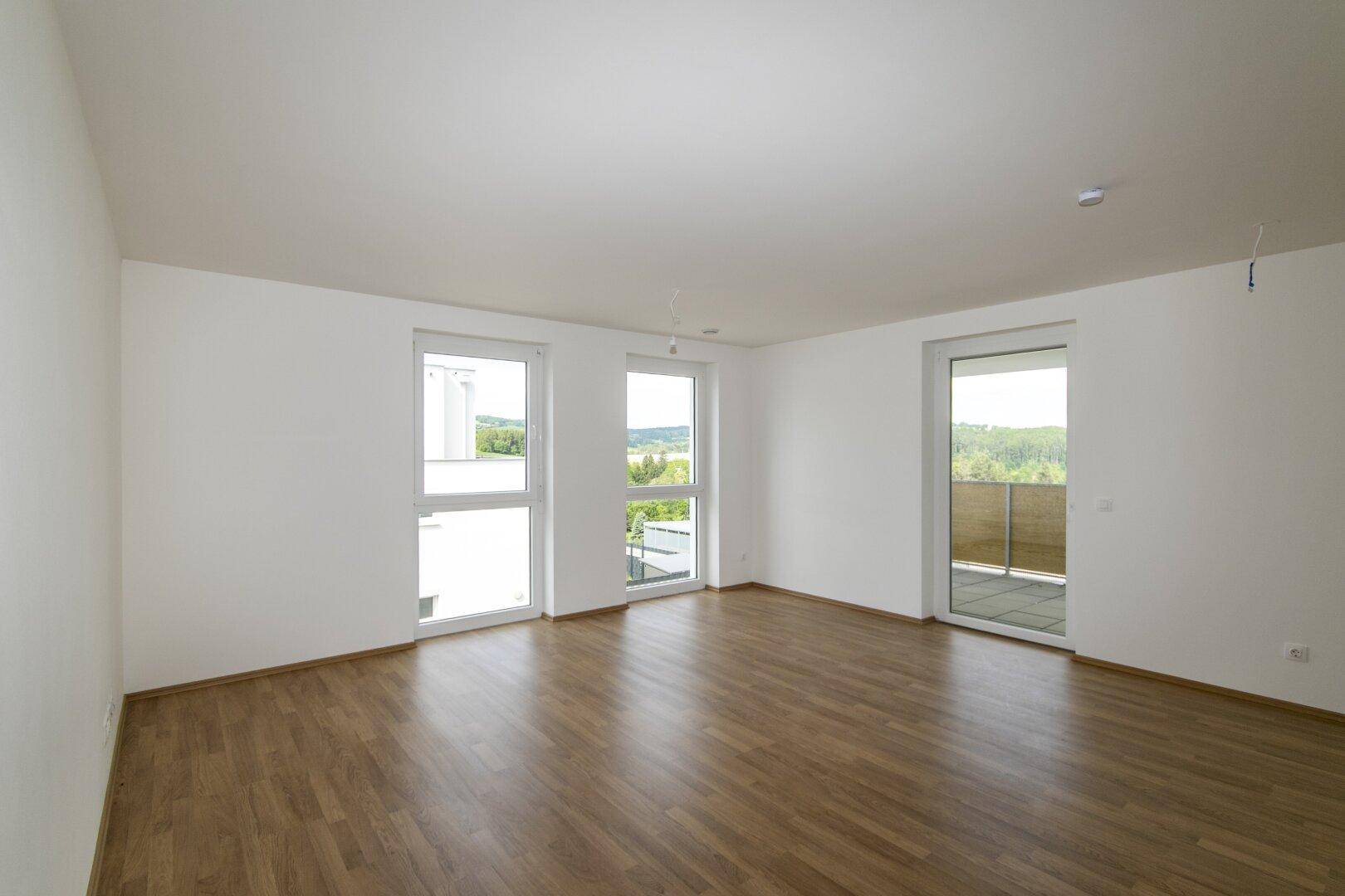 Helles, leeres Wohnzimmer mit großen Fenstern und Zugang zu einem Balkon, bereit zum Einzug.