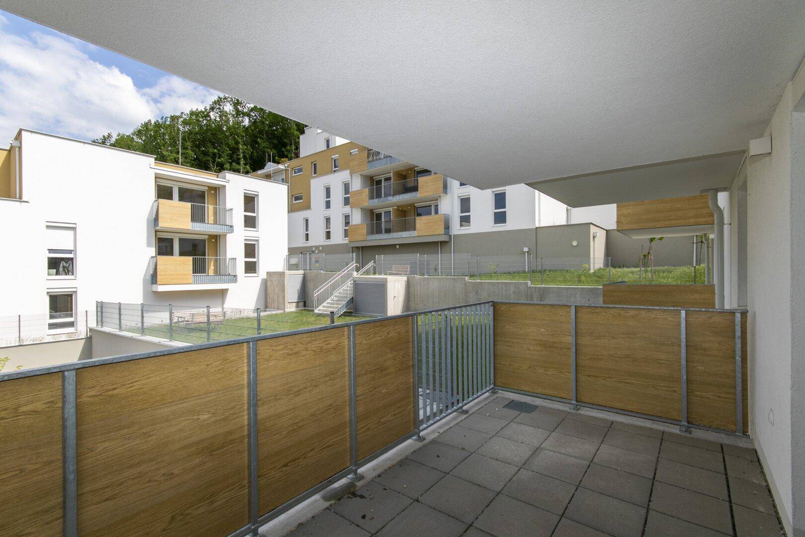 Balkon mit Holzsichtschutz und Blick auf die moderne Wohnanlage und die begrünte Umgebung.