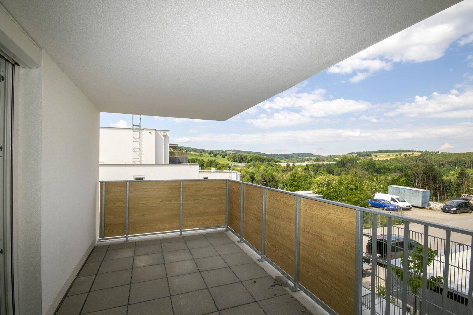 Heller Balkon mit Fliesenboden und Panoramablick über die grüne Hügellandschaft.