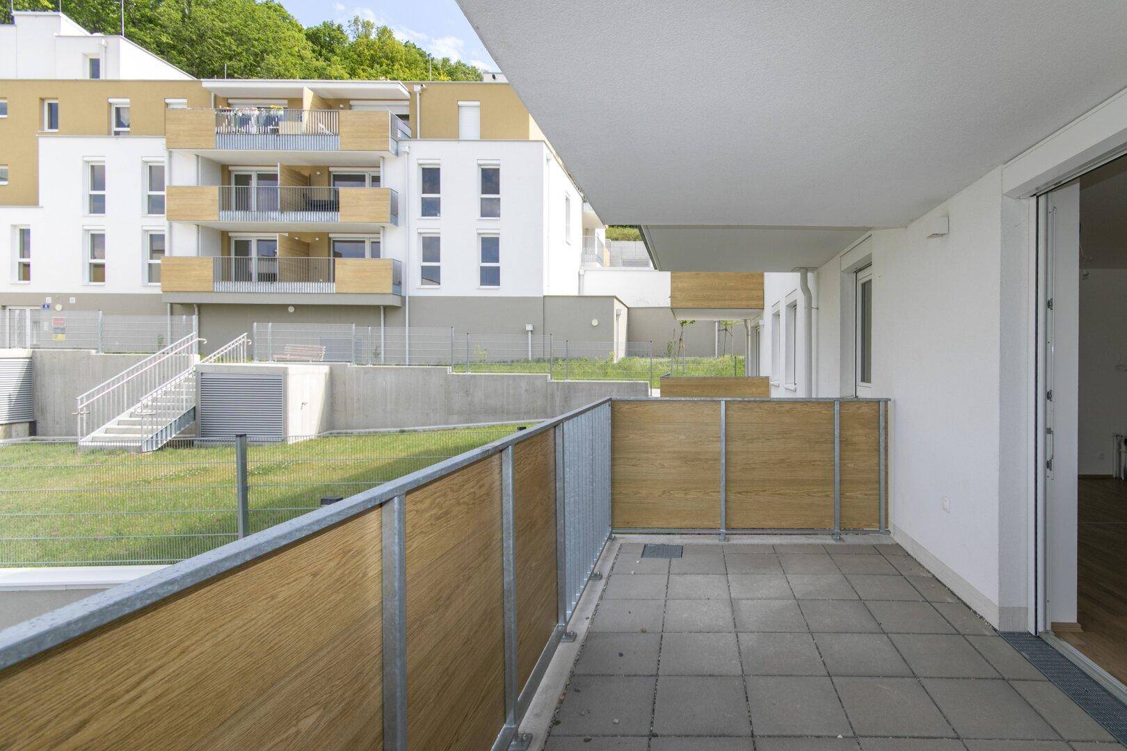 Heller Balkon mit Fliesenboden und Zugang zum Innenbereich, mit Blick auf die Neubauten.