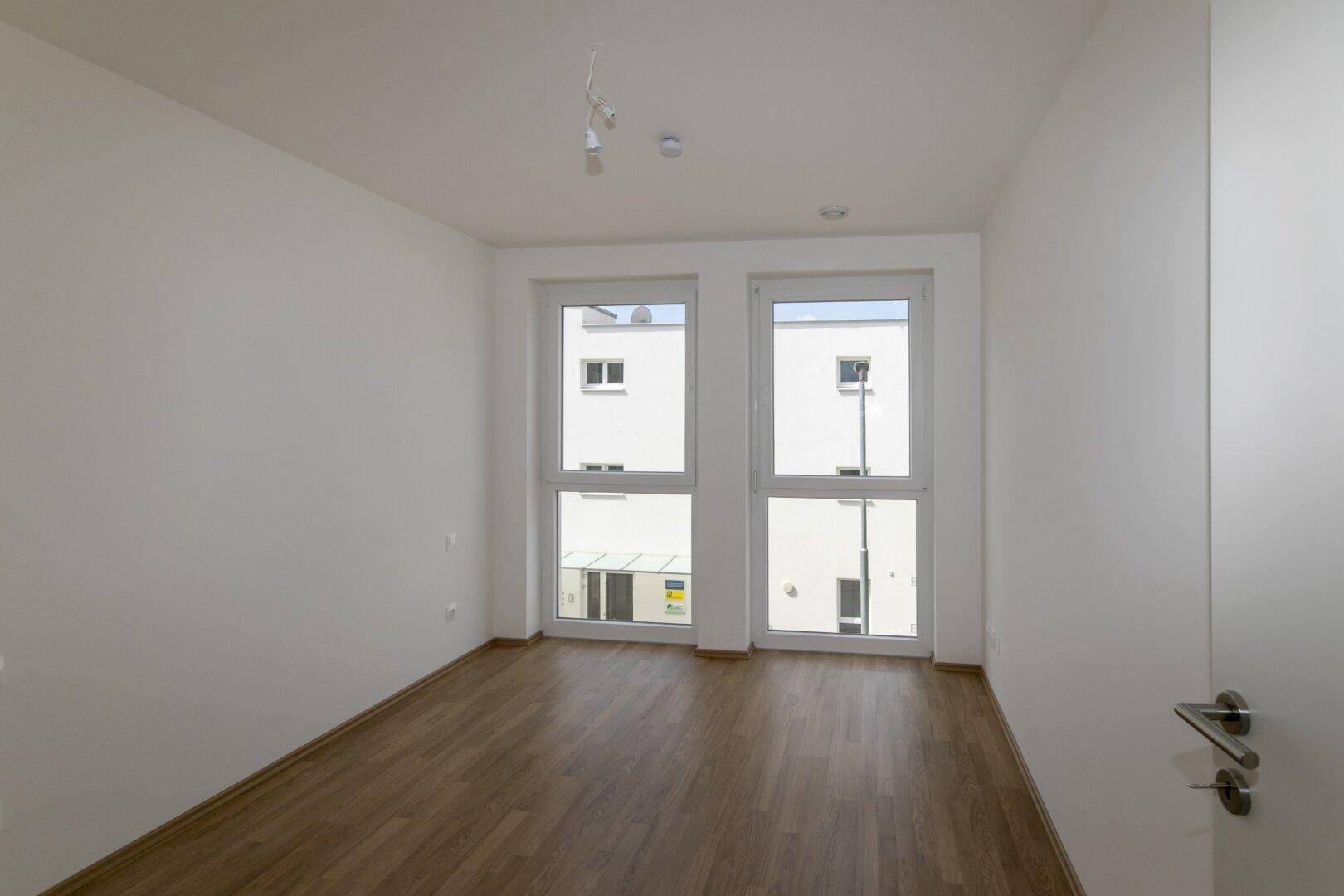 Helles Schlafzimmer mit großen Fenstern und Laminatboden, bereit zur individuellen Gestaltung.