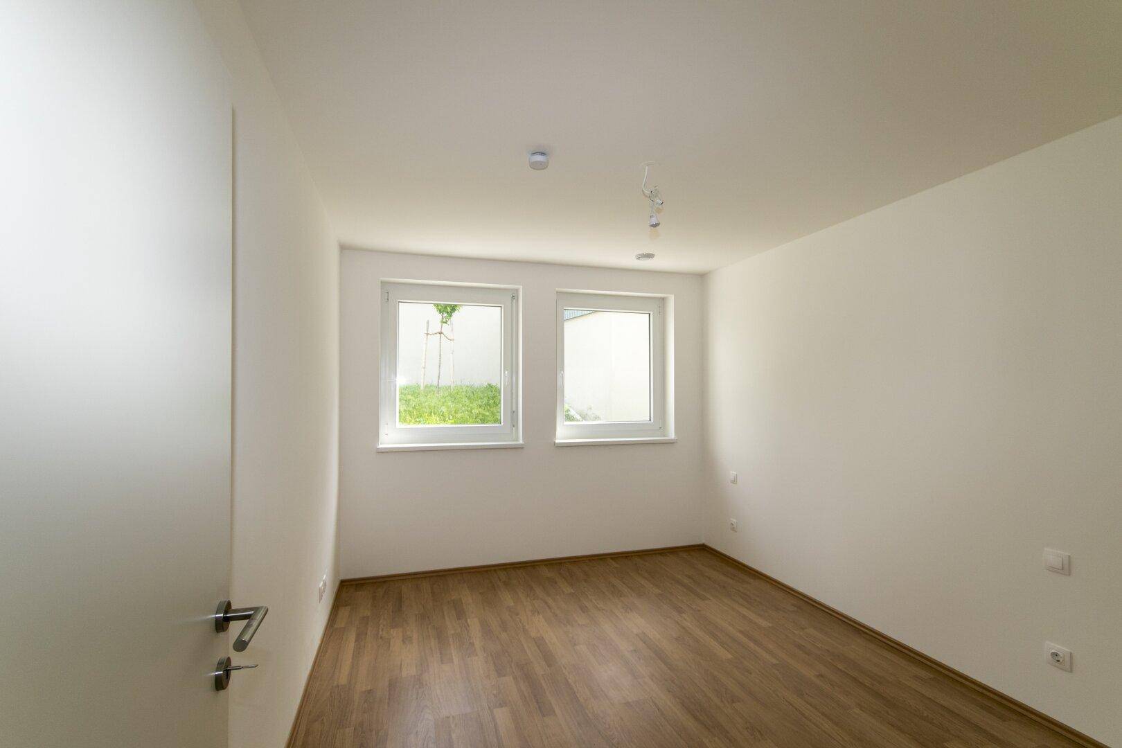 Helles Schlafzimmer mit Laminatboden und zwei Fenstern, ideal für individuelle Gestaltung.