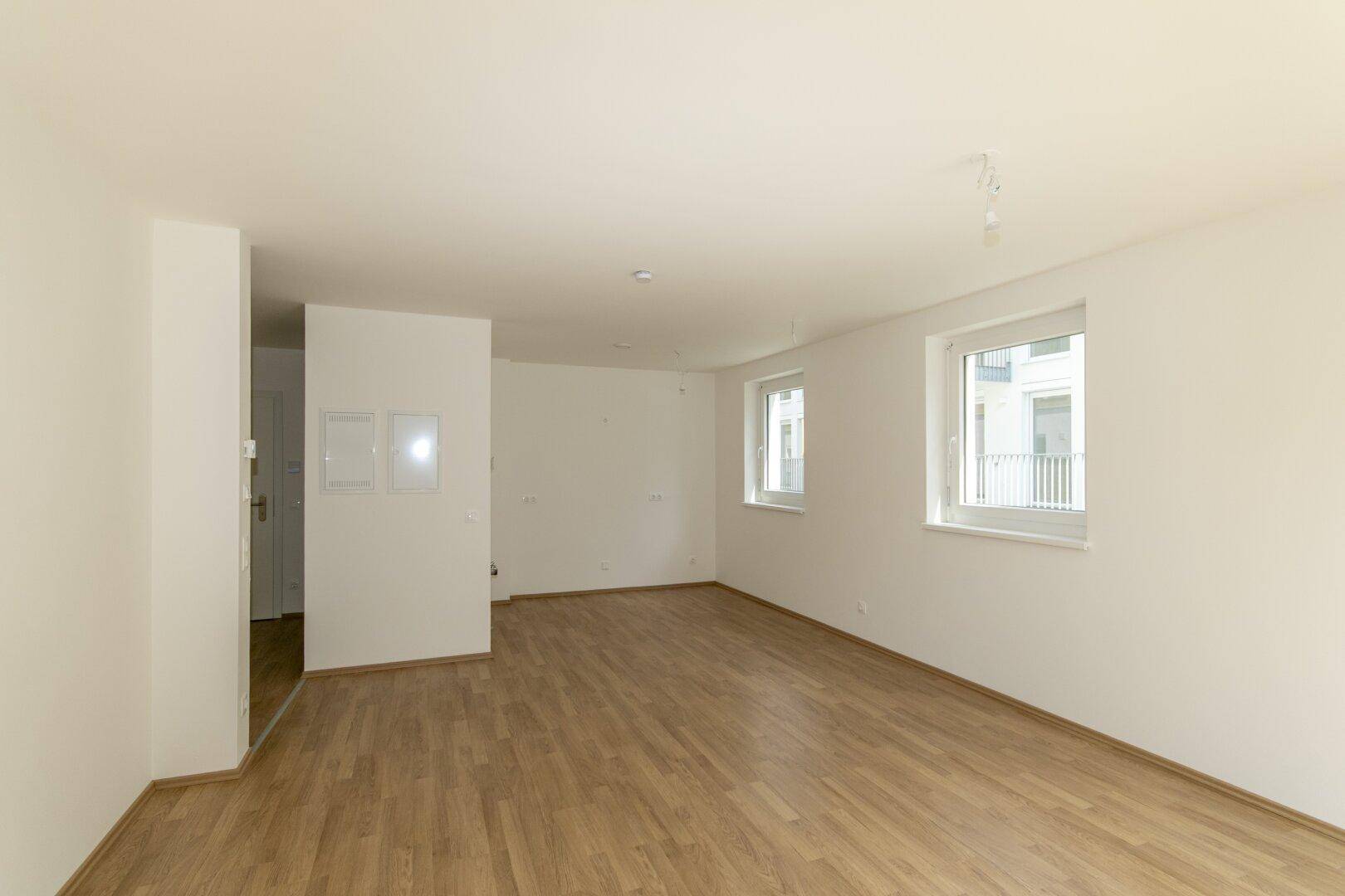 Geräumiger, heller Raum mit Laminatboden und mehreren Fenstern, bereit zur Einrichtung.